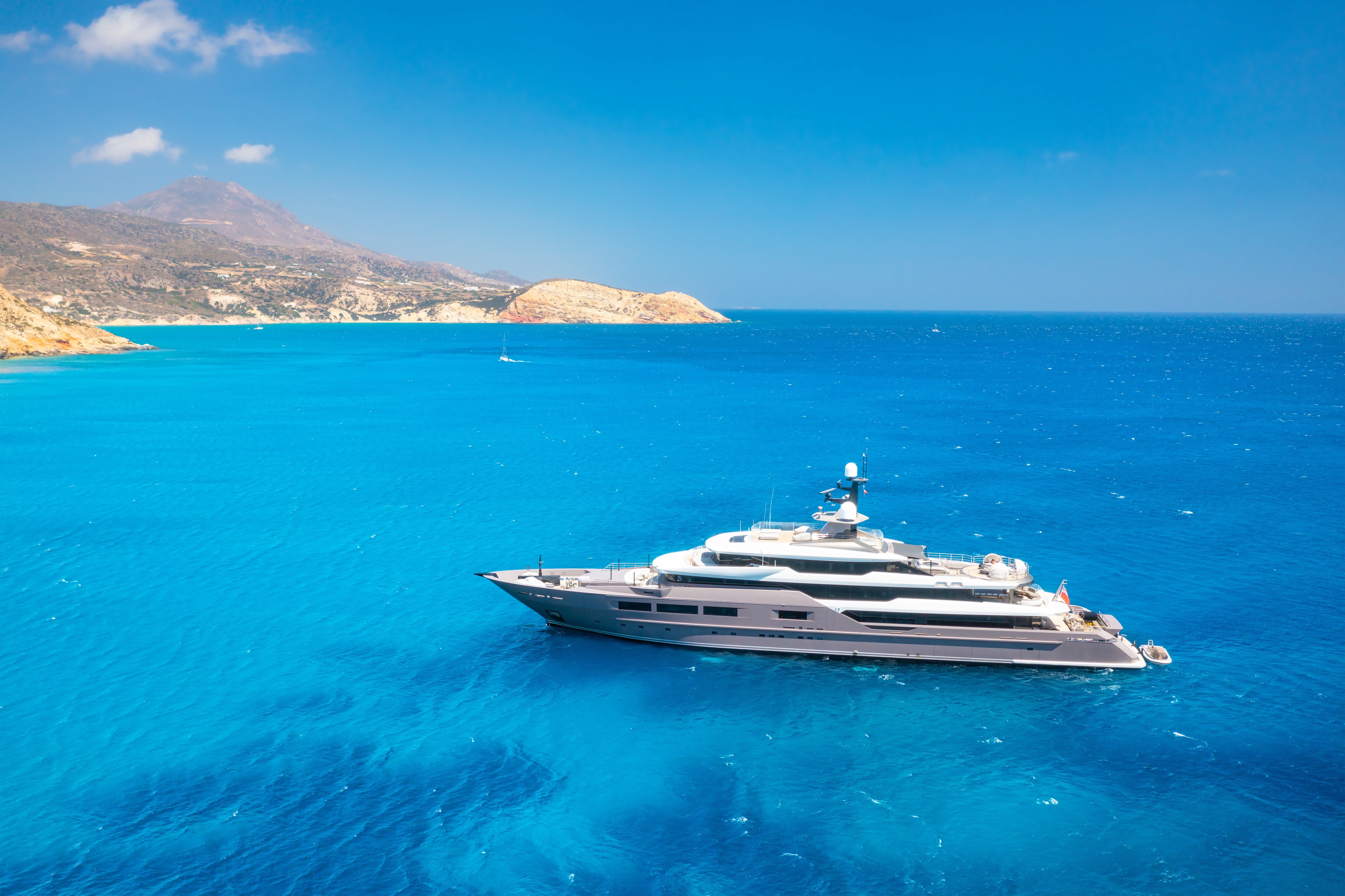 Aerial of a sleek superyacht in extraordinary turquoise Aegean water with arid coastline. Into the Blue