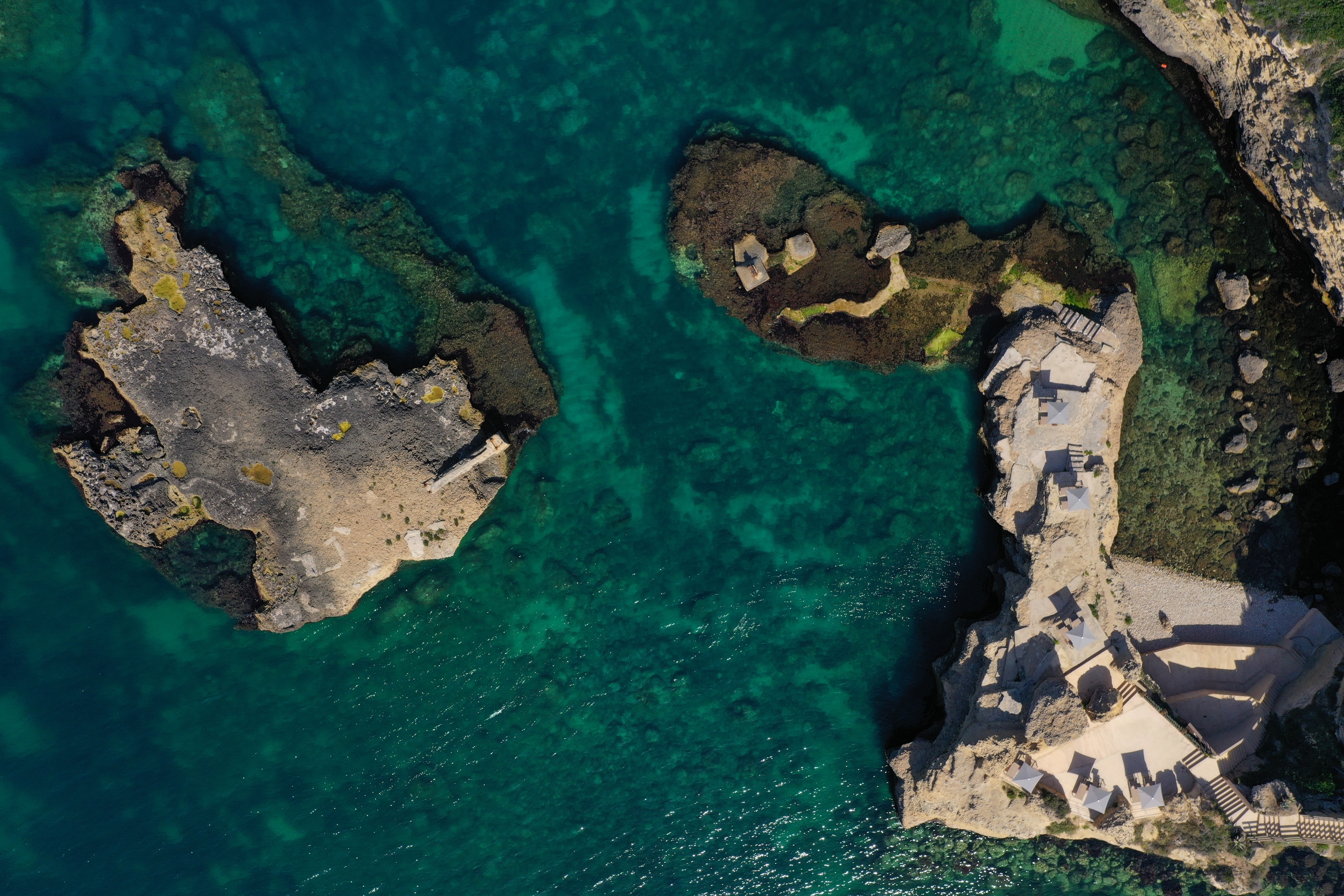 A rocky beach surrounded by dark emerald water, Sicily, Italy.