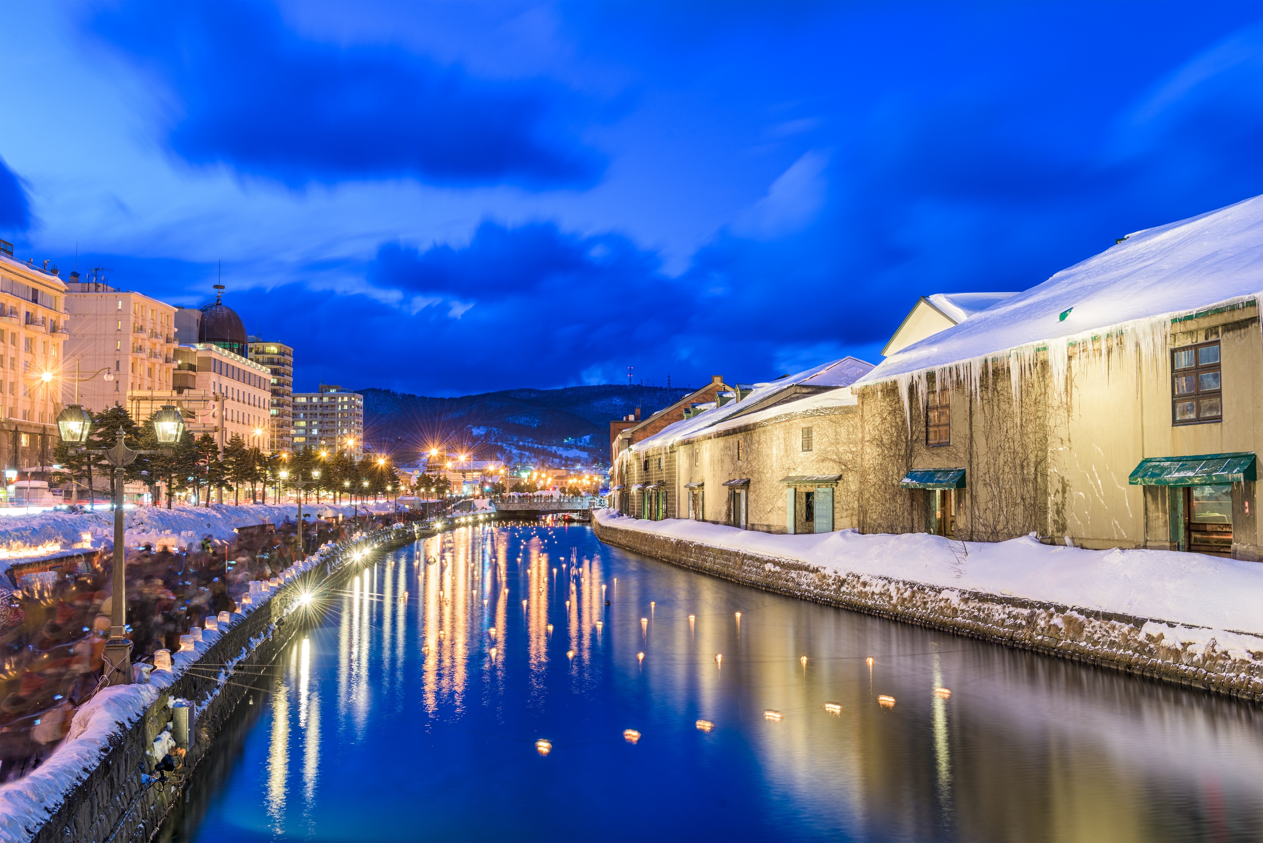 Hokkaido's Otaru canal in the winter with snowbanks along the edges and the night lights reflected in the water. Alps in Winter.