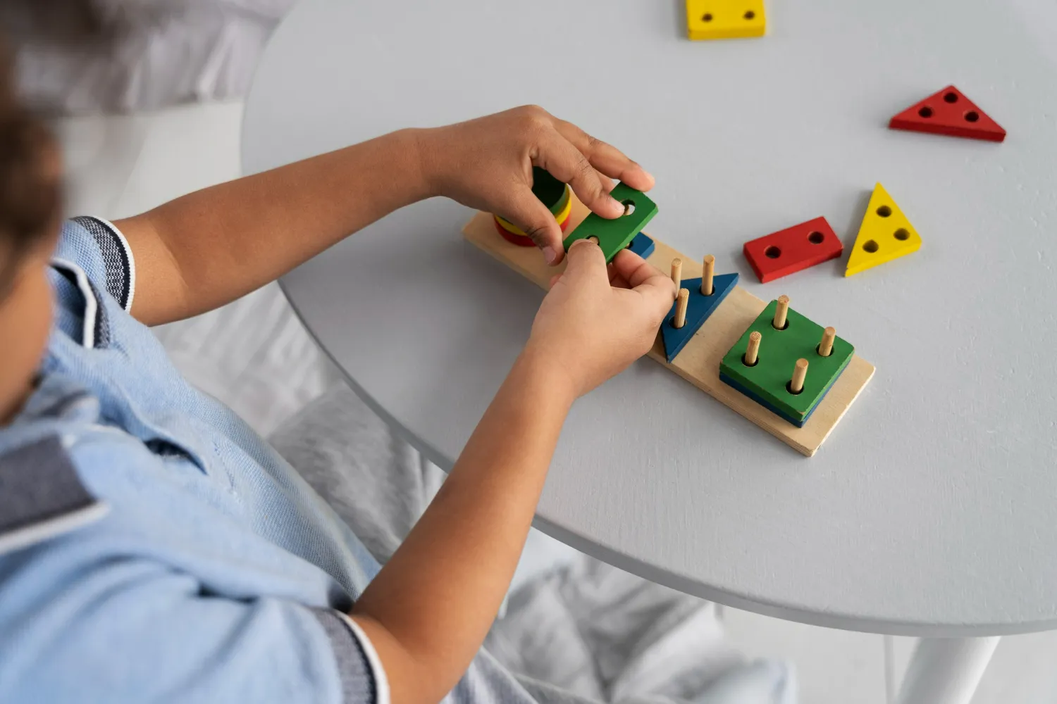 Child assembling colorful wooden shape sorting toy on a gray table.