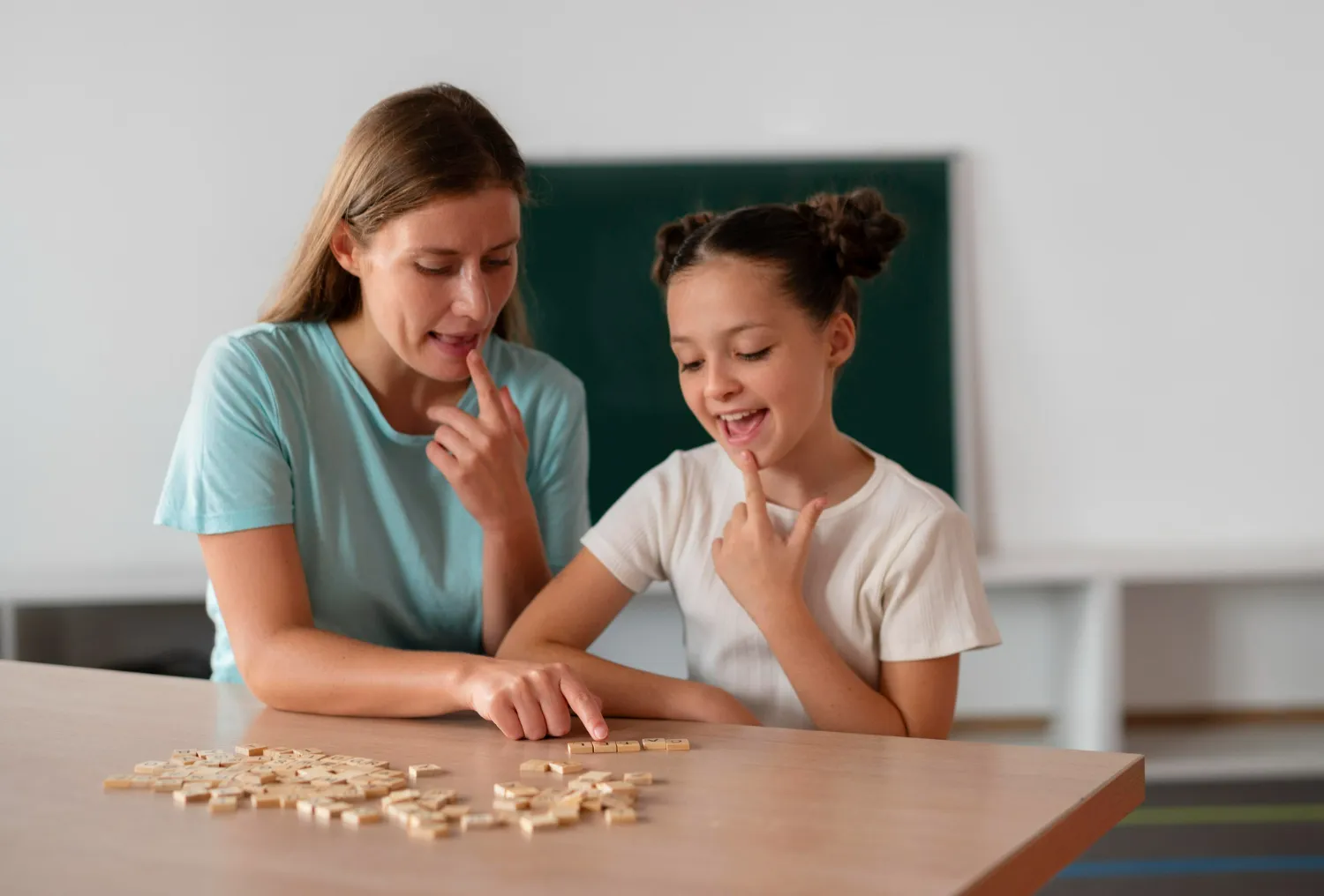 Woman and girl sitting at a table pointing at letter tiles, practicing speech or reading.