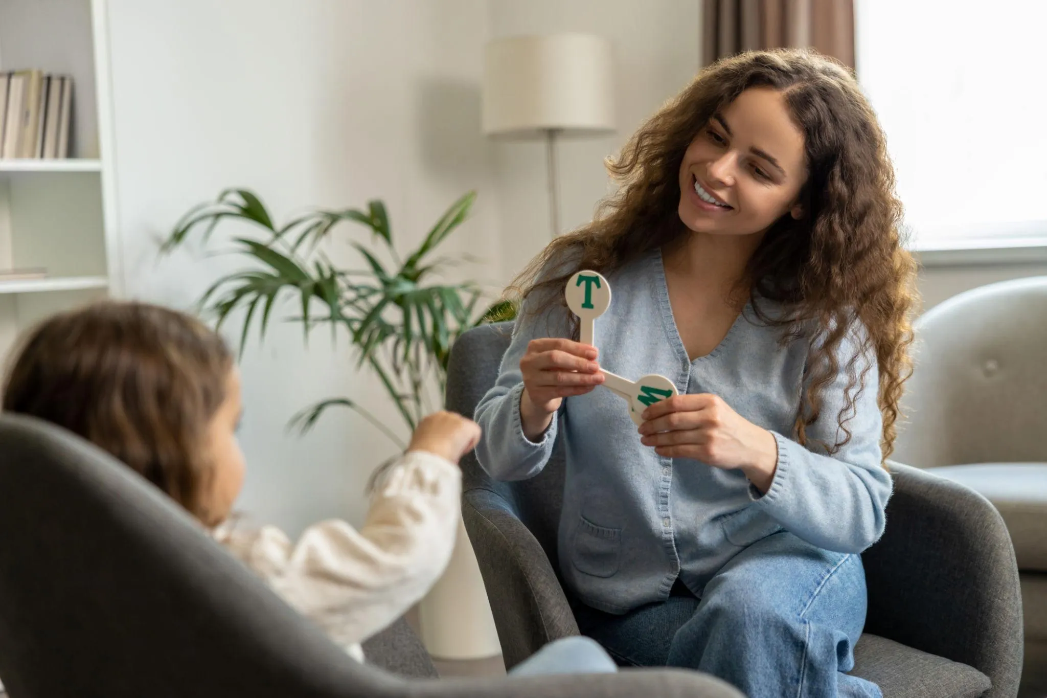 Woman showing letter cards to child during a speech therapy session in a cozy room.