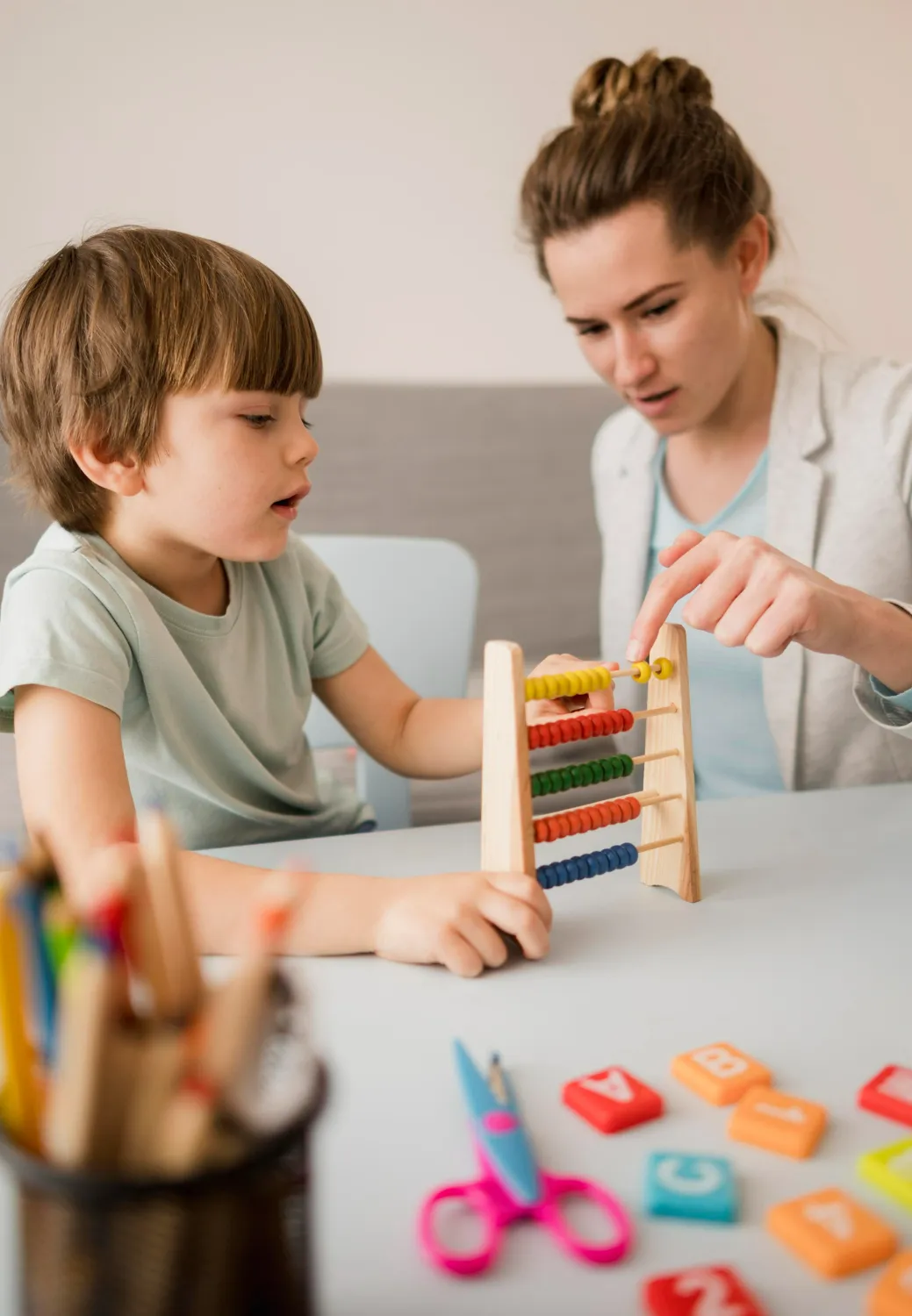 Child and woman using a wooden abacus for learning at a table with colorful supplies.
