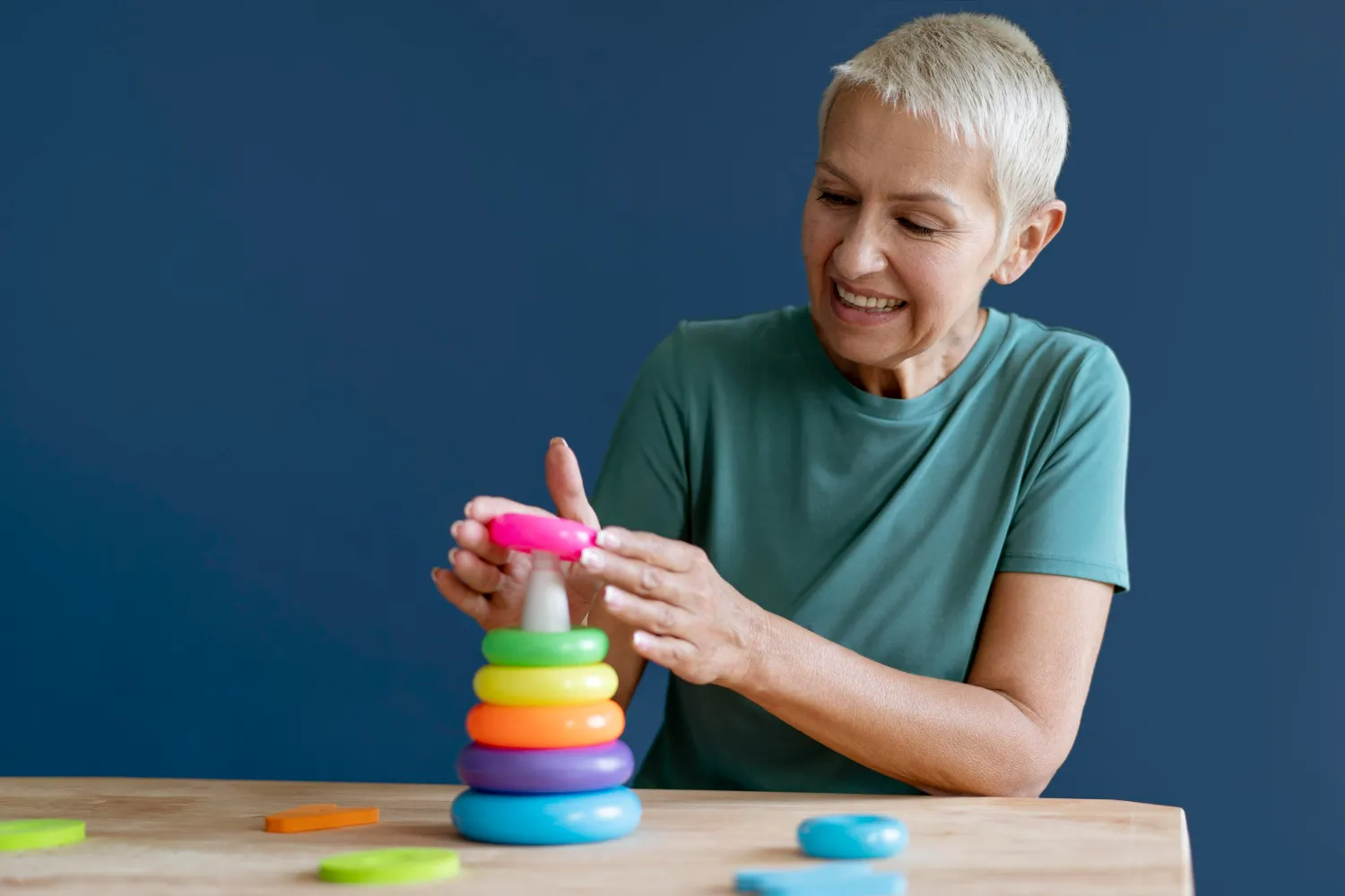 Smiling woman stacking colorful rings on a plastic cone toy against blue background.
