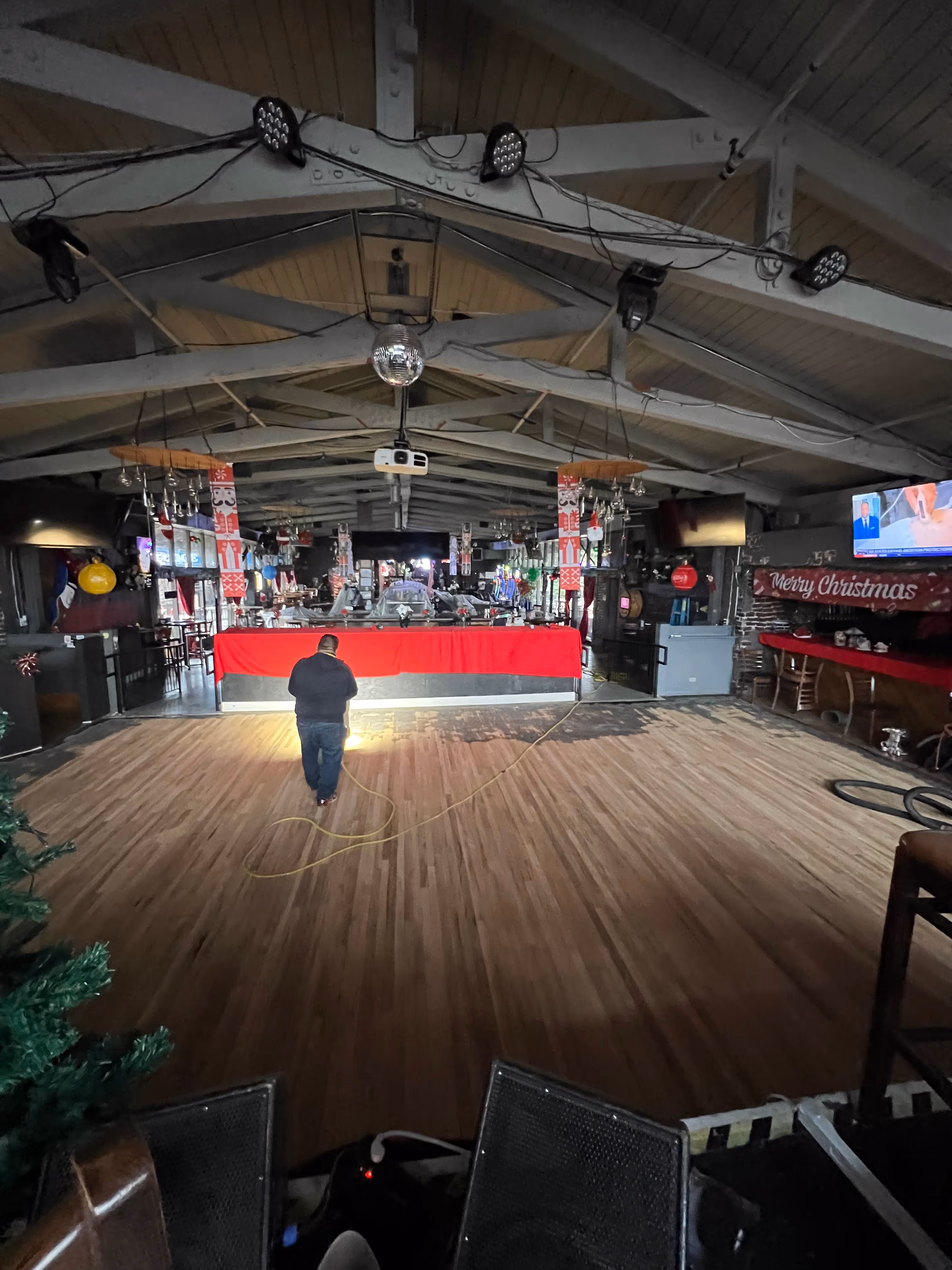 Person standing on a wooden floor facing a bar covered with a red cloth in a decorated room.