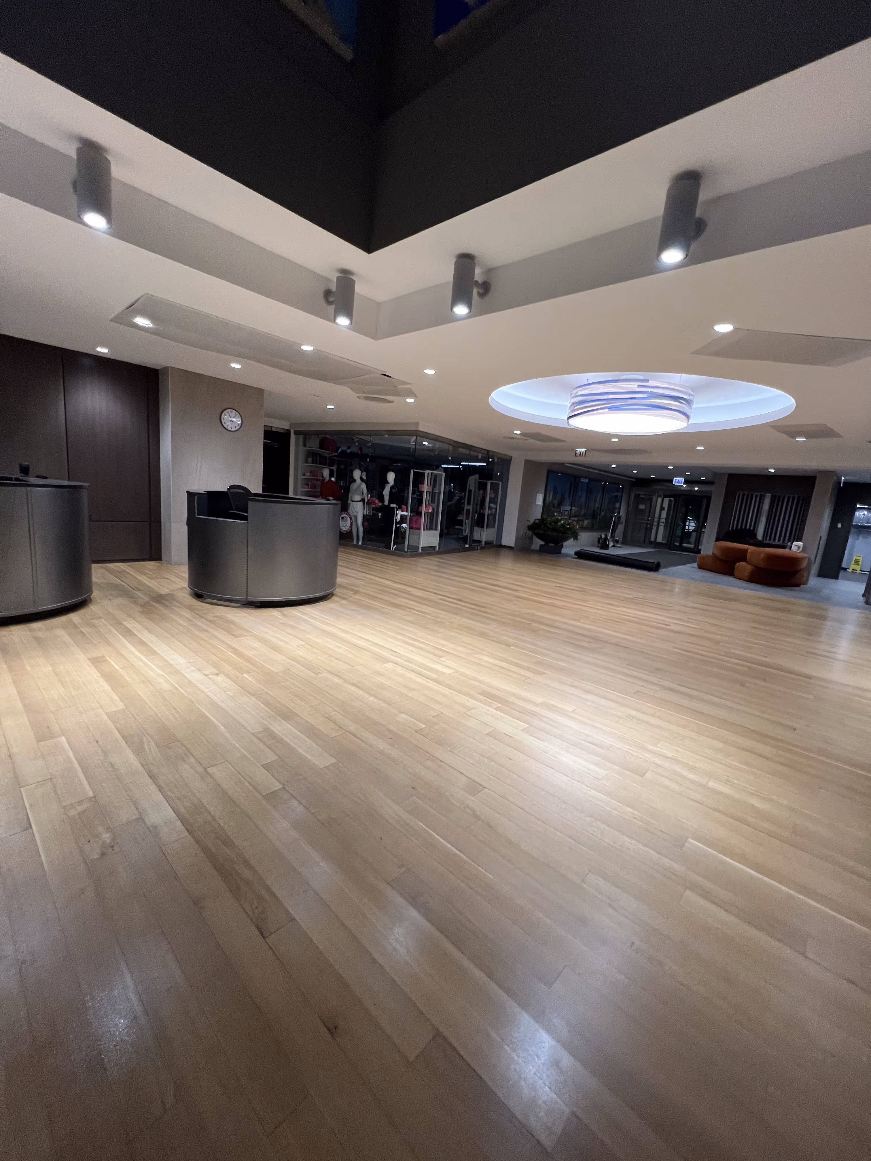 Spacious modern lobby with wooden floor, round reception desks, ceiling lights, and seating area.