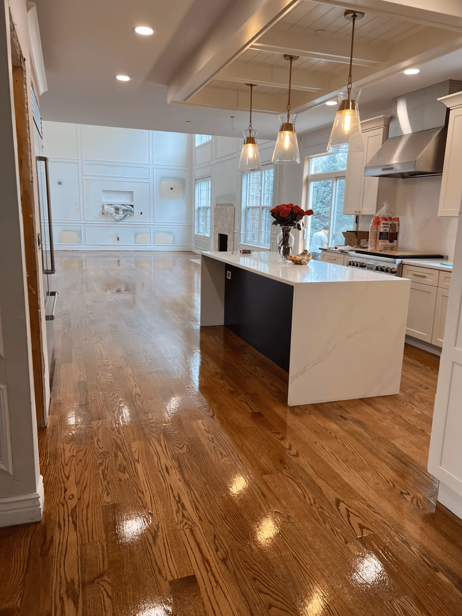 Modern kitchen with shiny hardwood floors, white cabinets, island, pendant lights, and large windows.