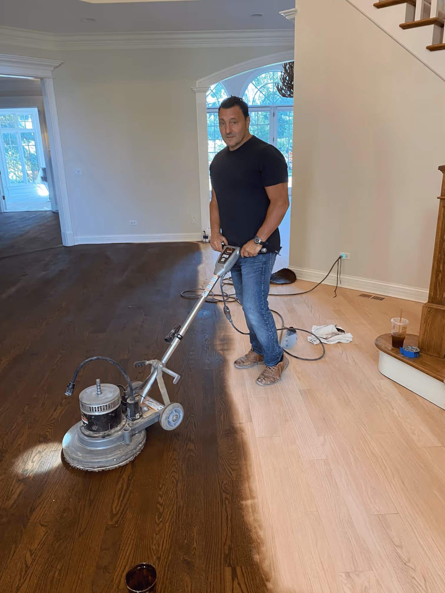 Man standing on a hardwood floor using a floor polishing machine to darken and refinish the wood.