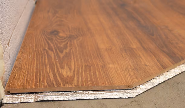 Close-up of layered wood flooring with soundproof underlayment on concrete floor.
