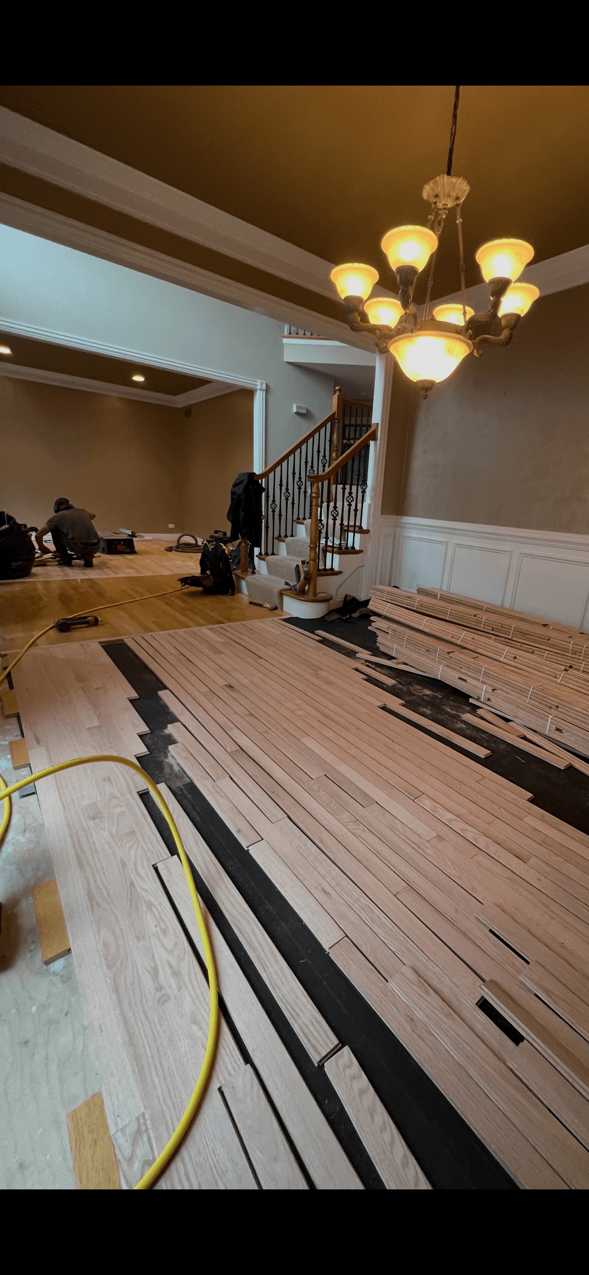 Large empty room with parquet floor and ceiling lights, two workers cleaning near end by windows.