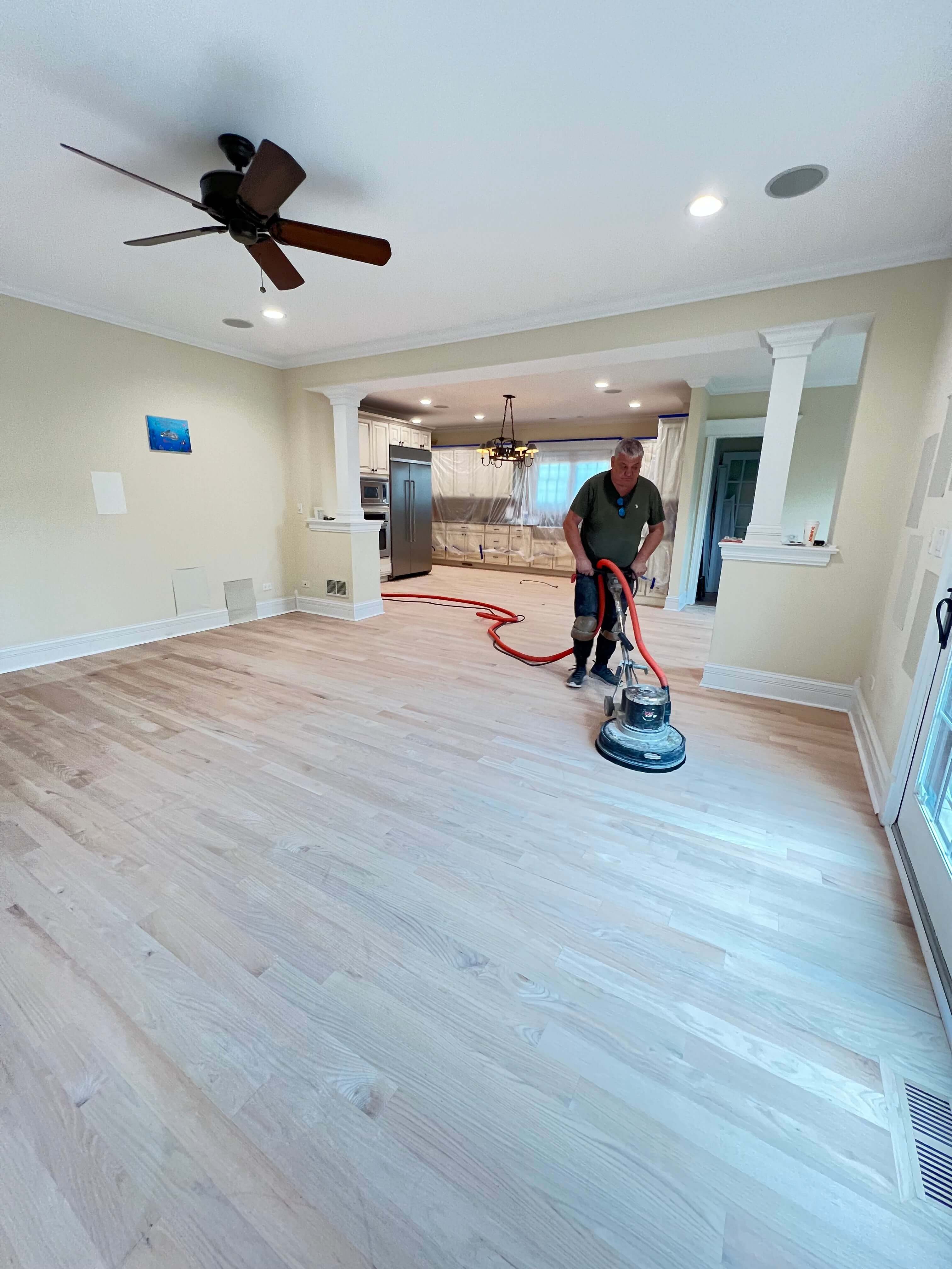 Empty modern room with light wood floor, dark kitchen island, staircase, and blue LED ceiling lights.