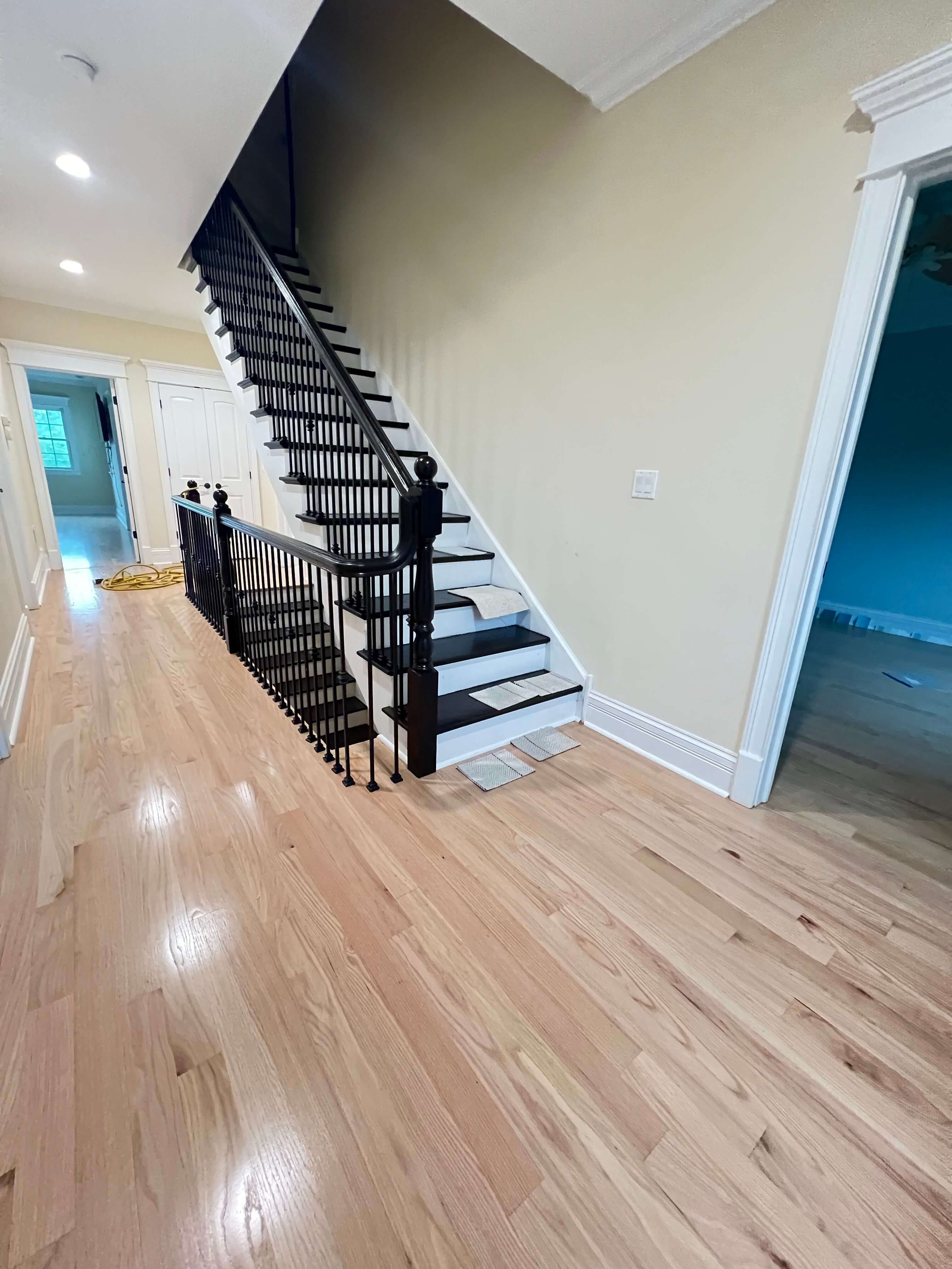 Man using floor buffer to polish wooden floor in a large kitchen with dark cabinets.