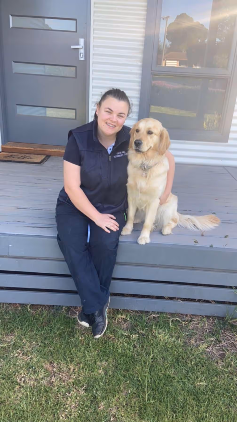 Woman sitting on outdoor wooden steps next to a golden retriever dog, both looking at the camera.