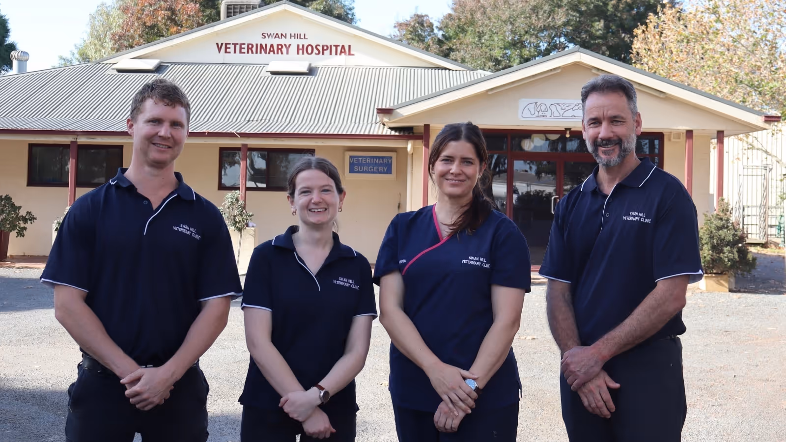 Four smiling veterinary staff in navy uniforms standing outside Swan Hill Veterinary Hospital.