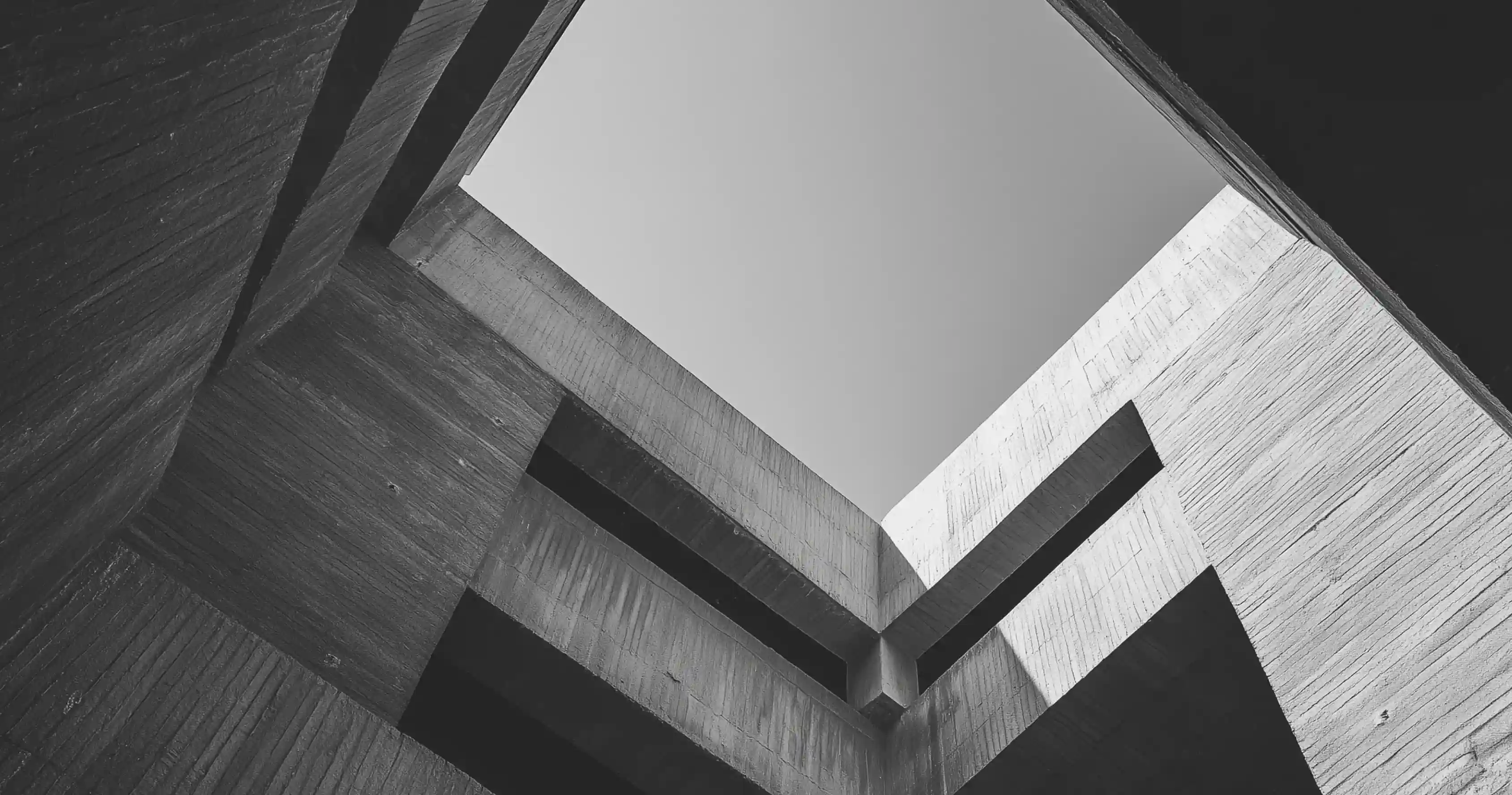 Black and white photo of intersecting concrete building walls taken from below with sky visible above.