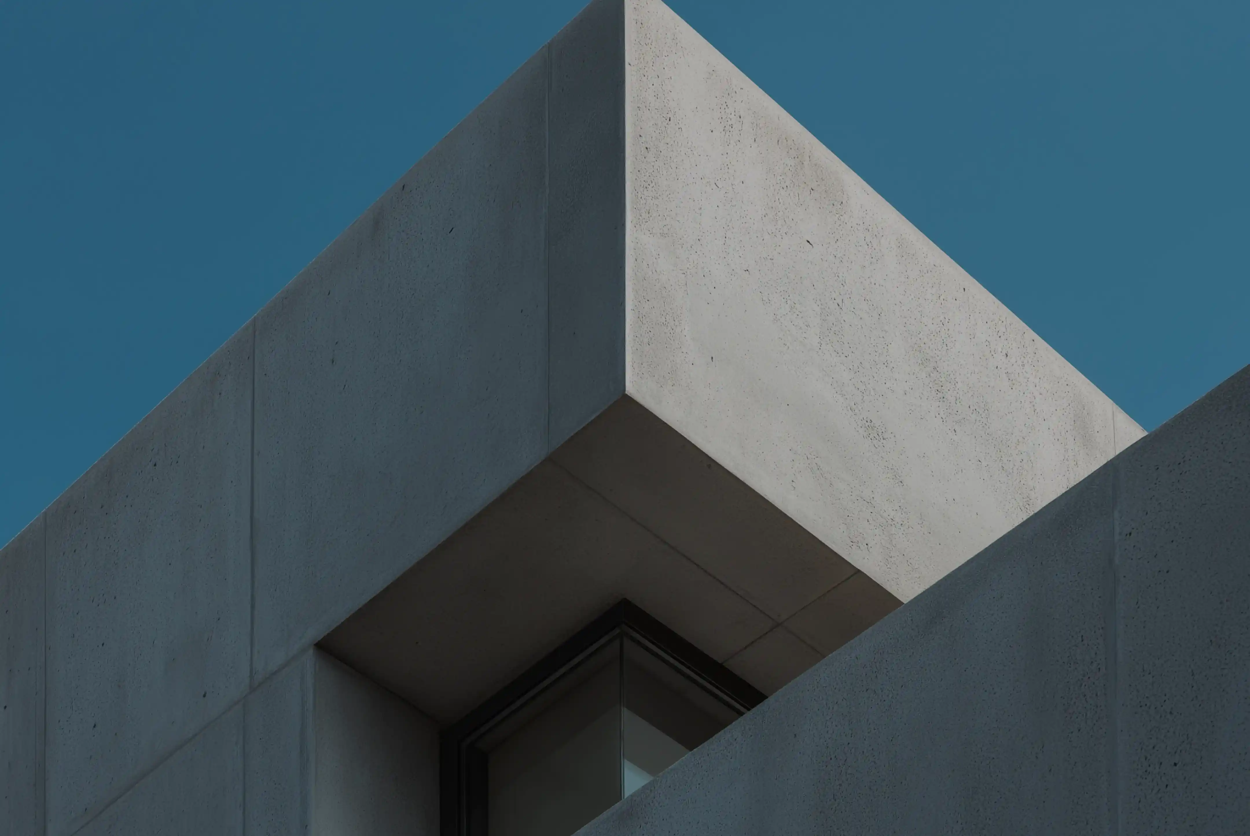 Corner of a modern concrete building with sharp edges against a clear blue sky.