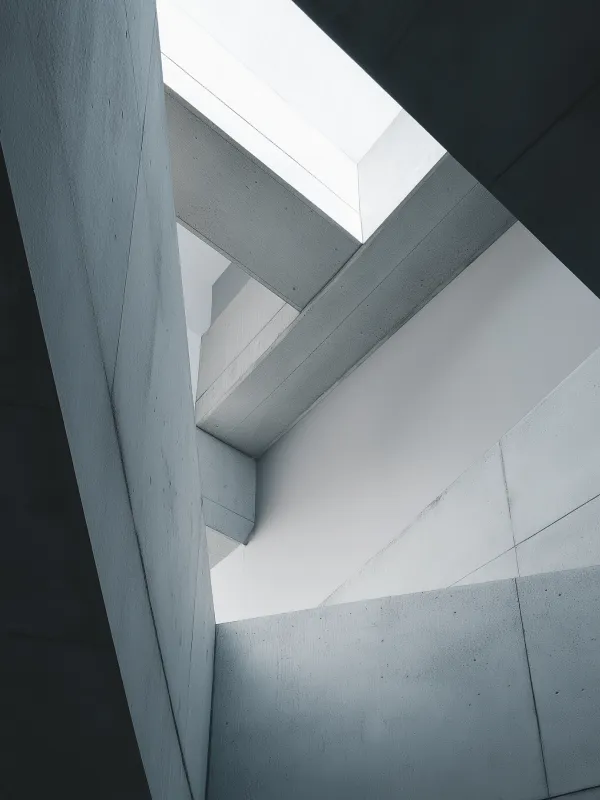 Abstract view of concrete beams and walls with light coming through an angular opening above.