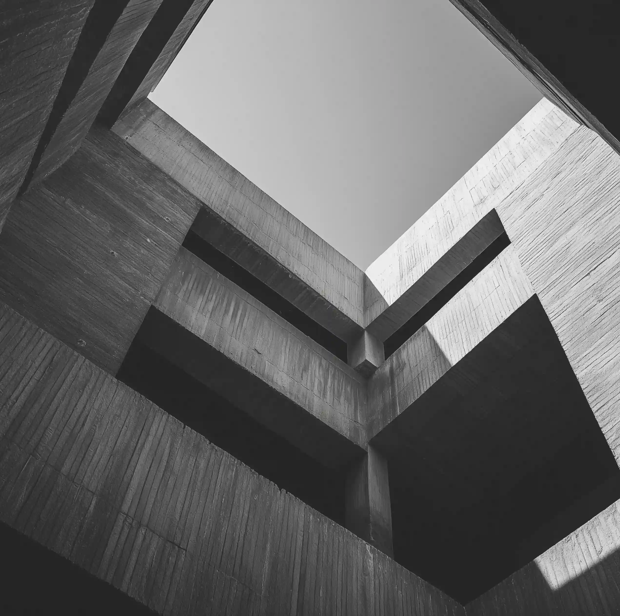 Black and white photo of a modern concrete building's angular interior courtyard with shadow patterns.