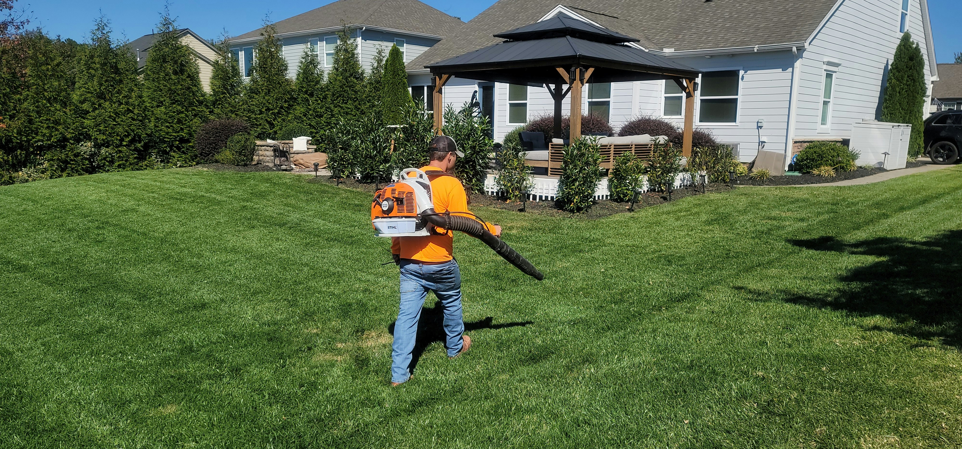 Gärtner mit Stihl Rucksack-Laubbläser pflegt grünen Hausgarten mit Pavillon