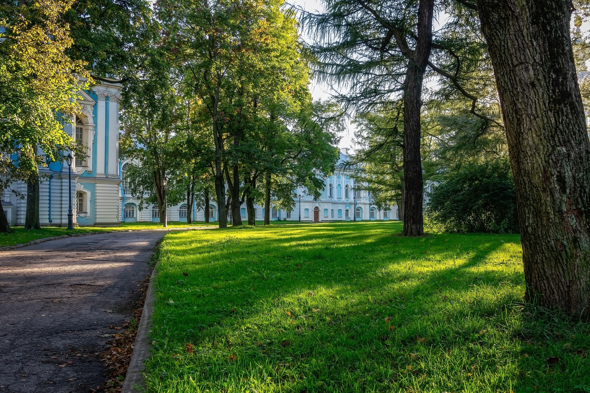 Gepflegter grüner Rasen mit Bäumen vor einem historischen blau-weißen Gebäude im Park