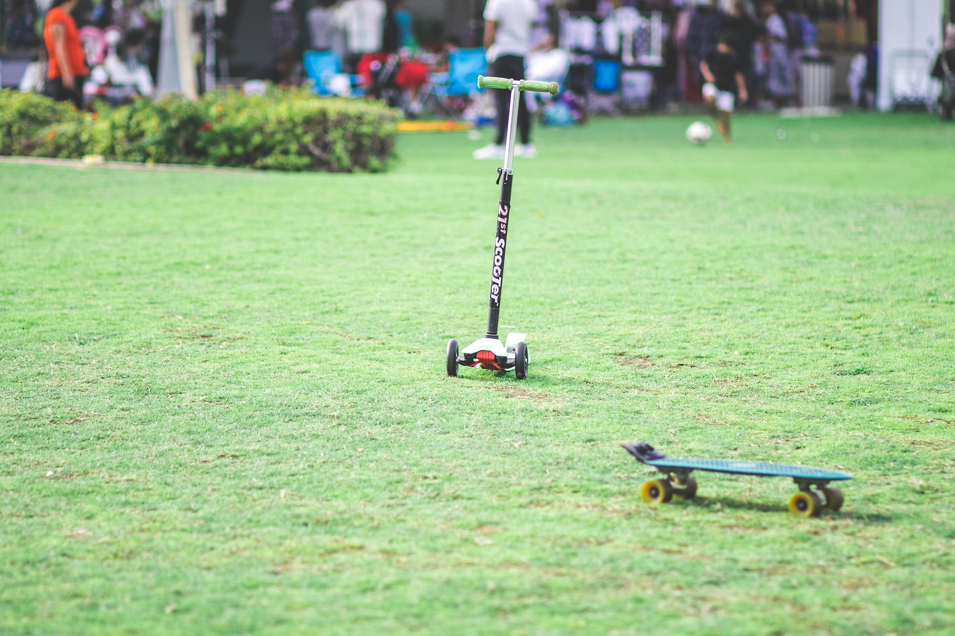 Kinder-Tretroller und Skateboard liegen auf gepflegtem Rasen im Park