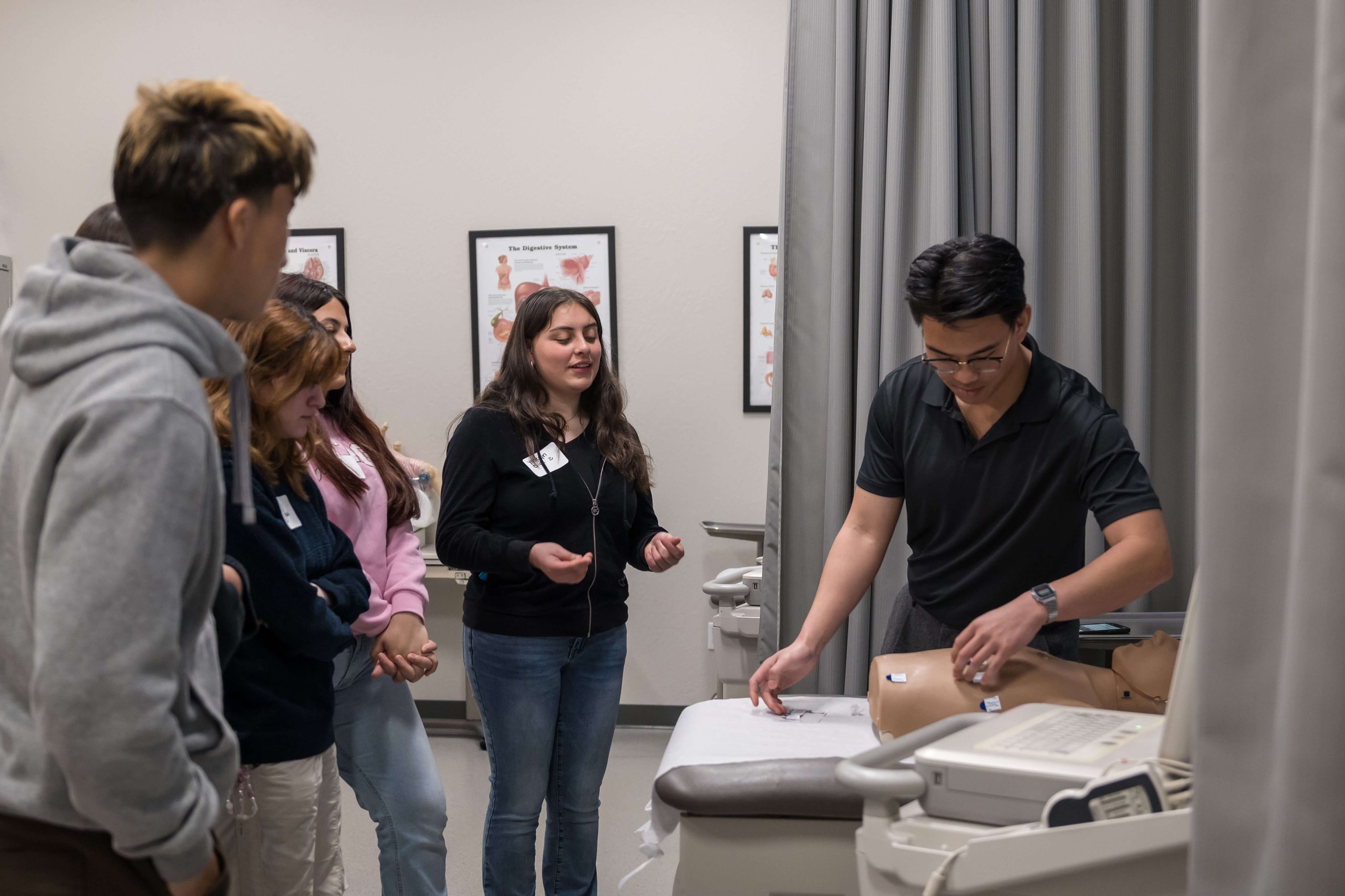 Group of young people observing a man demonstrating on a medical training mannequin in a clinic room.