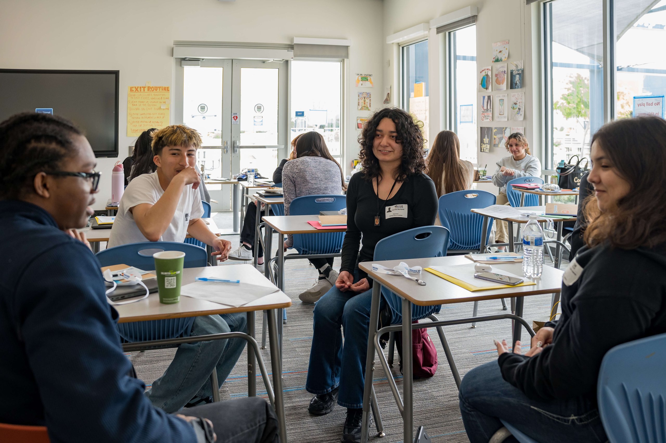 A diverse group of students sitting at desks in a classroom engaged in conversation and study.