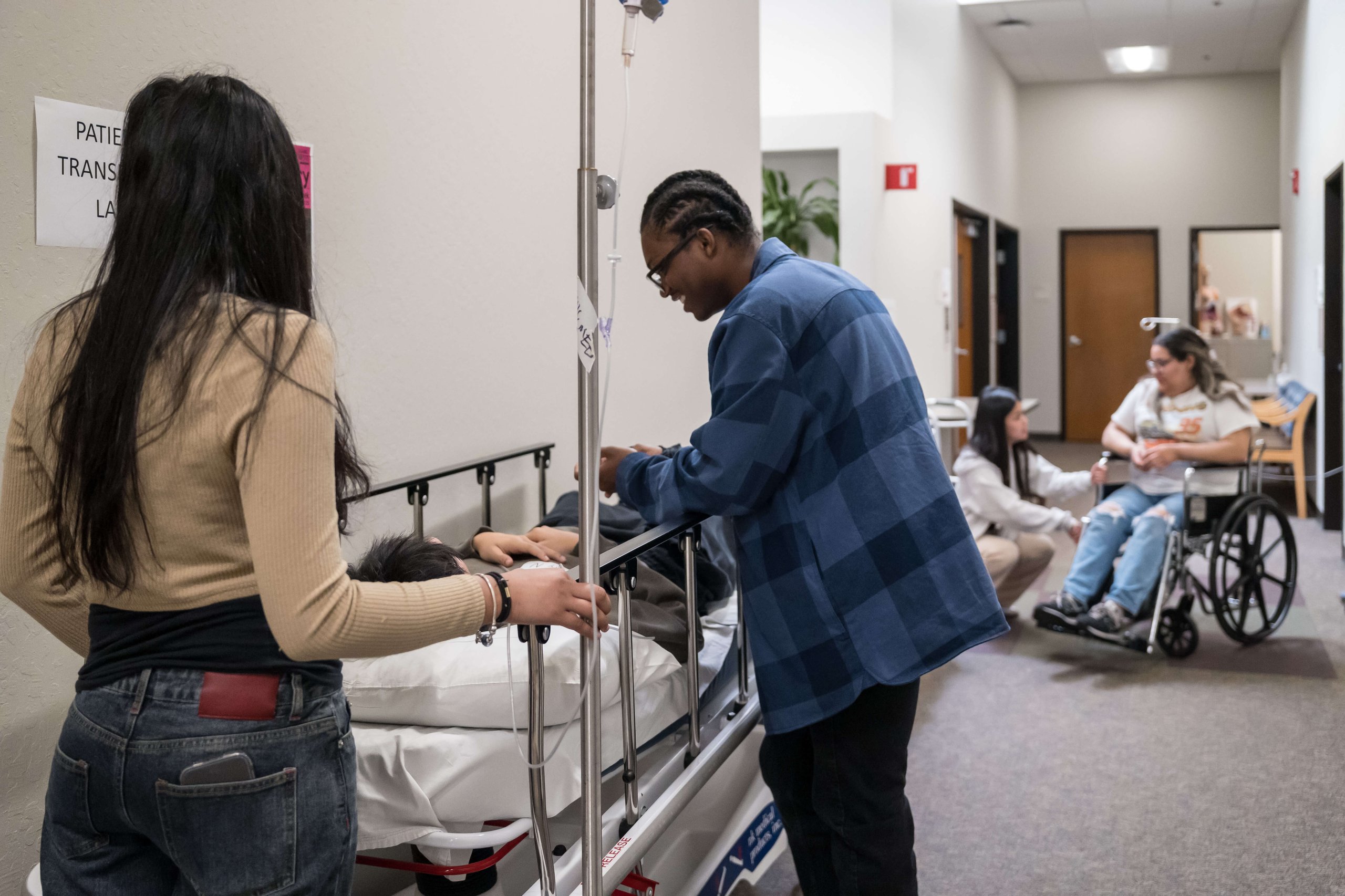 Student assisting with a patient care simulation using a hospital bed and IV stand in a clinical training setting.