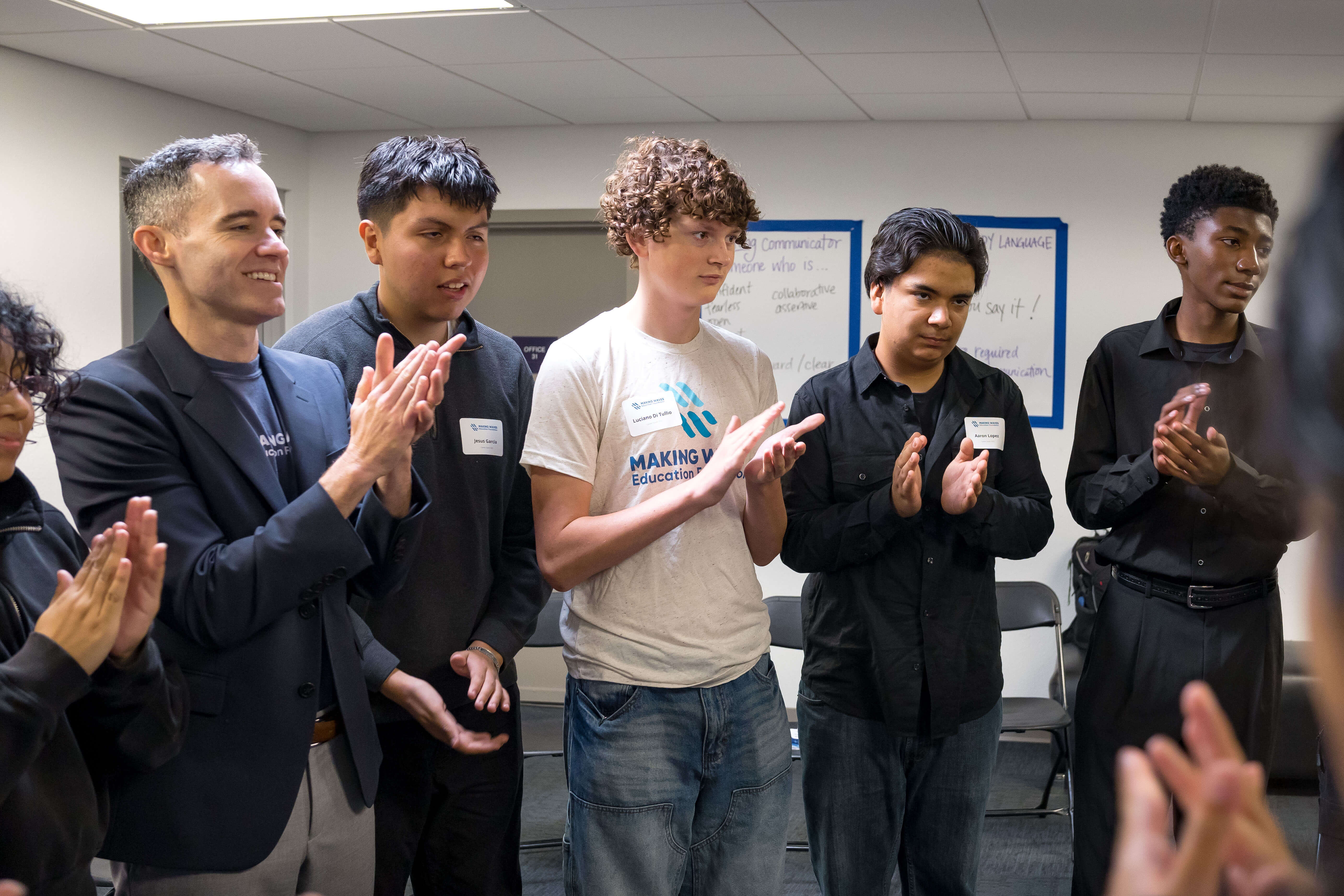 A group of people standing in a room clapping, some wearing name tags and casual clothes.