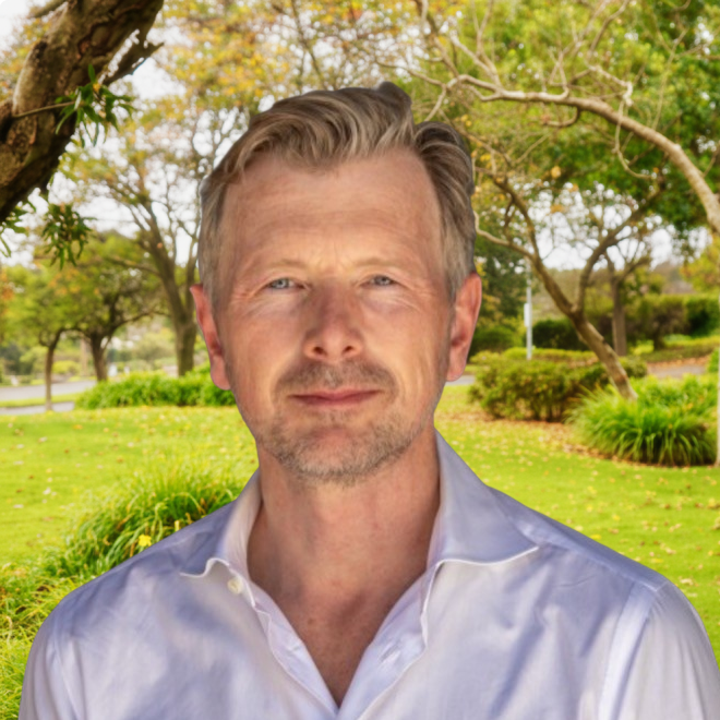 Middle-aged man with light brown hair wearing a white shirt standing in a green park.