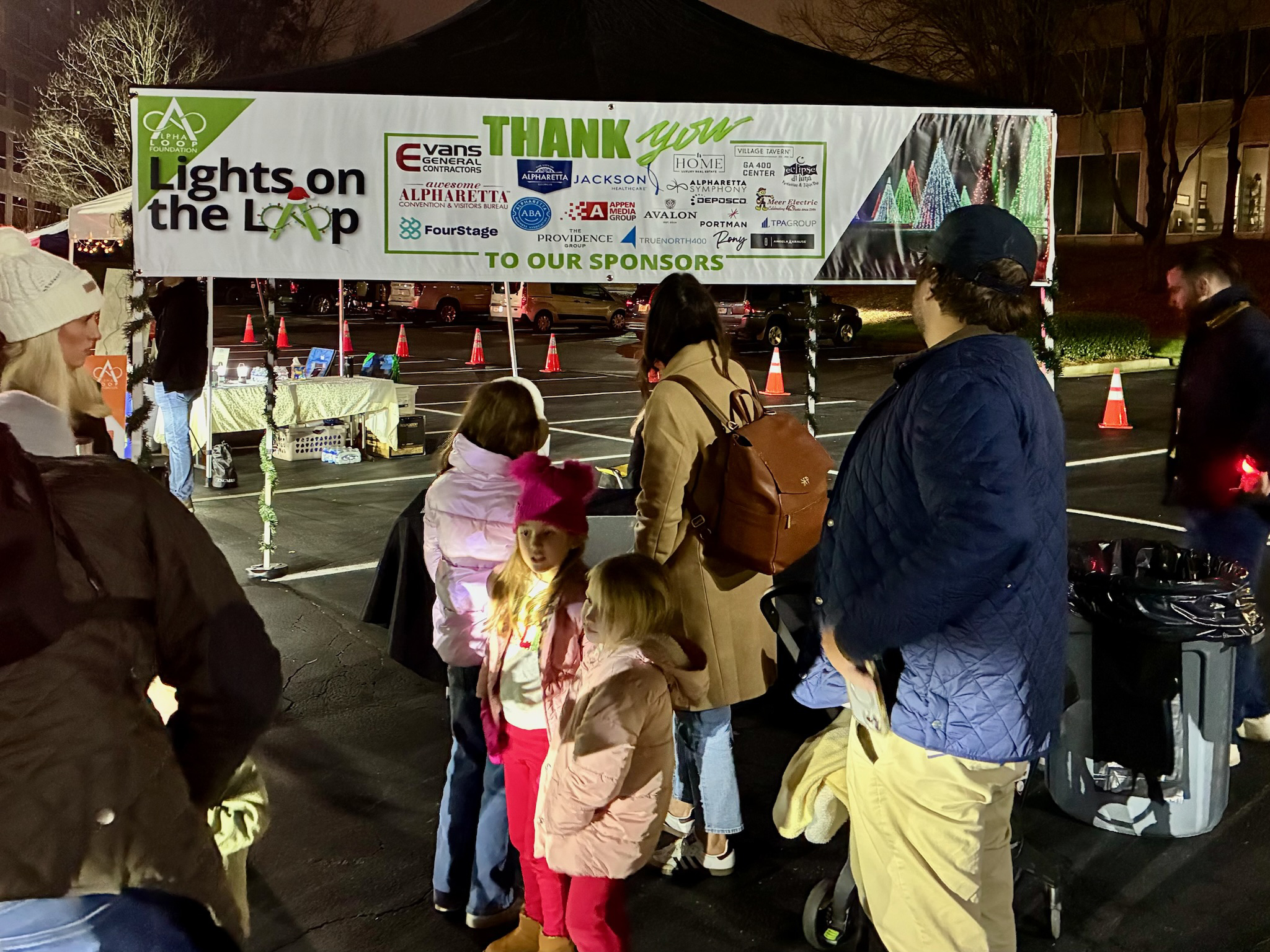 Families gather beneath the Lights on the Loop sponsor banner at Alpha Loop Foundation’s 2025 event in Alpharetta.