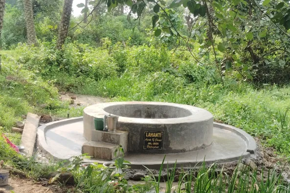 Concrete well structure surrounded by greenery with two metal containers on its edge.