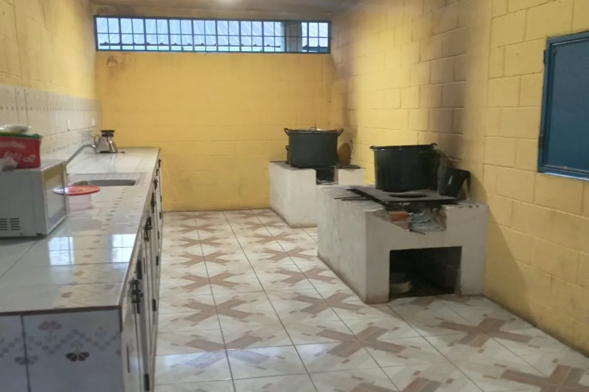 Simple kitchen with yellow walls, tiled floor, concrete wood stoves, and a countertop with a sink and microwave.
