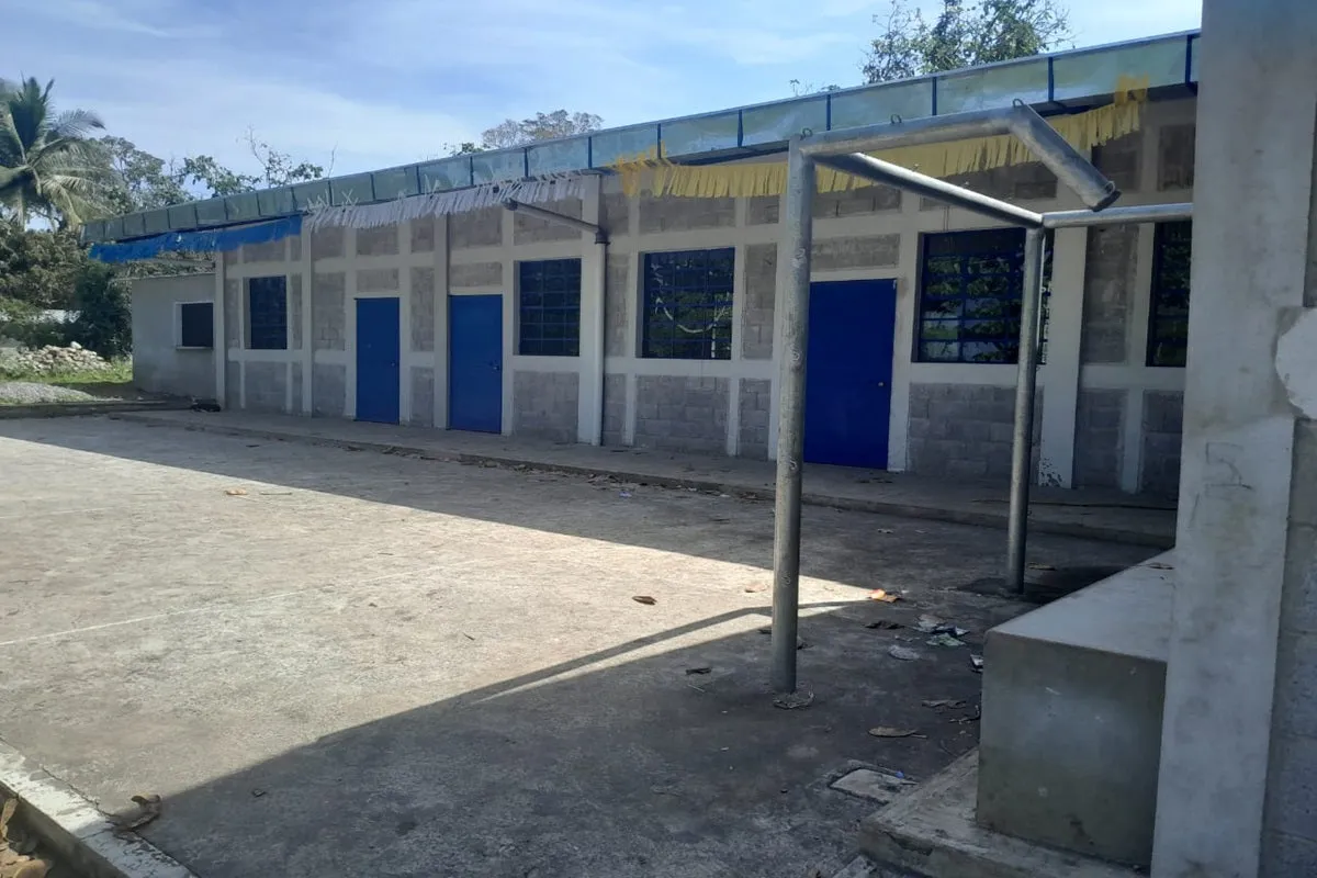 Concrete building with blue doors and windows next to a paved yard under a blue sky.