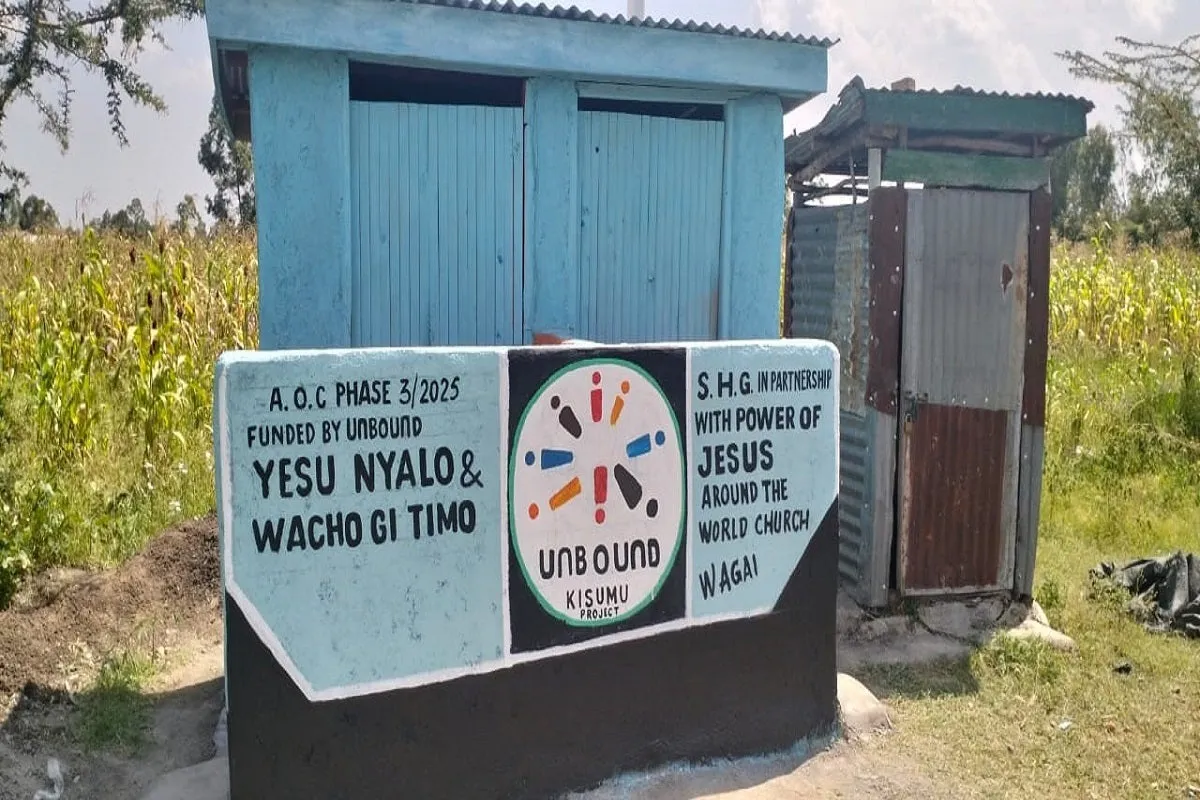 Two blue-painted pit latrines with a sign showing Unbound funding and church partnership in Kisumu, Kenya.