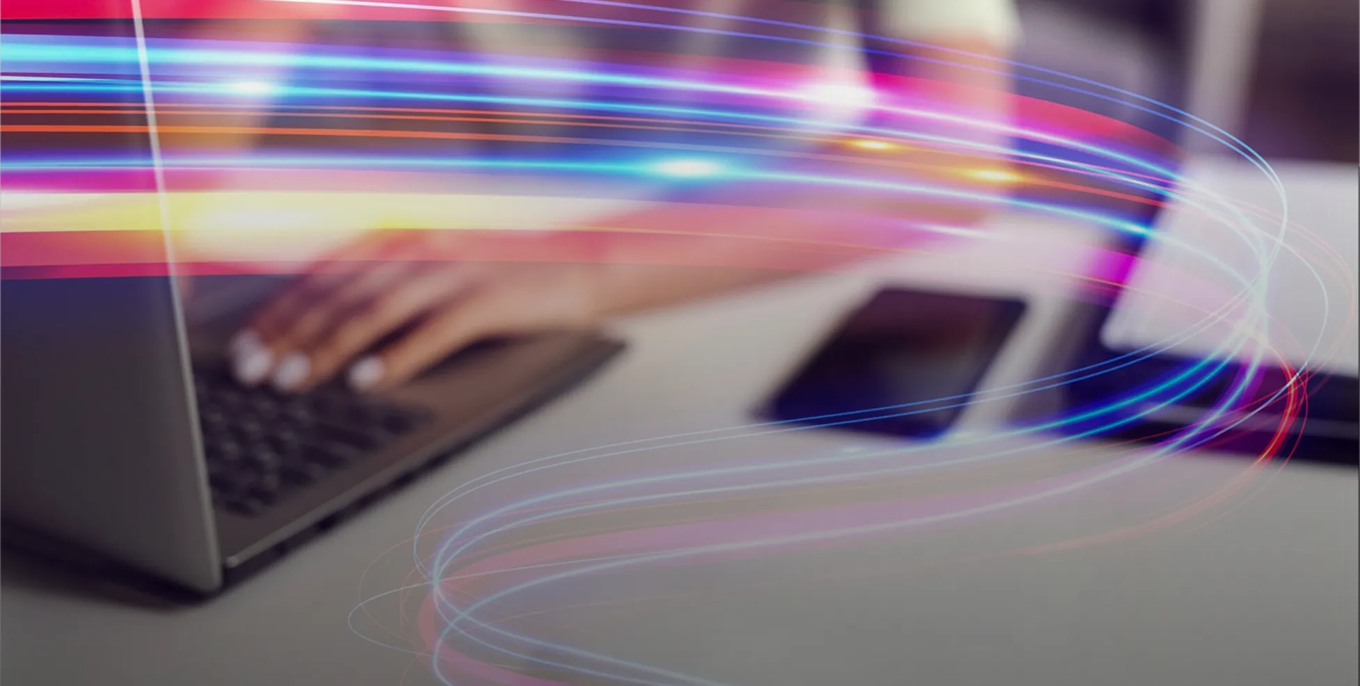 Hand typing on laptop keyboard beside a smartphone with curved colorful light trails overlay.