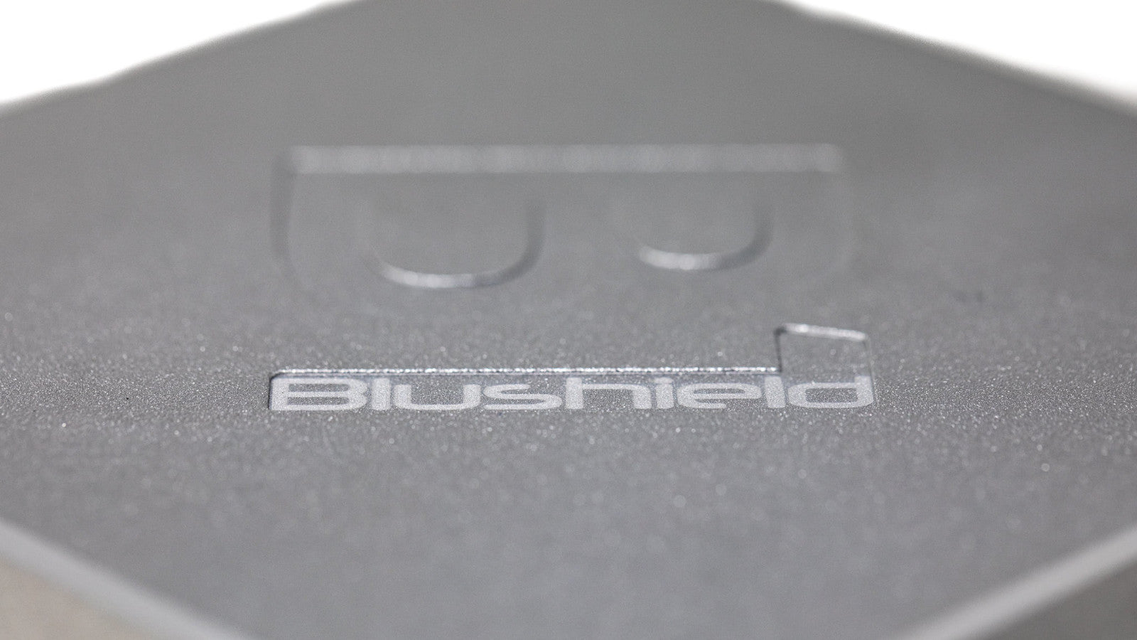 Close-up of matte metallic surface with the word Blushield embossed on it.