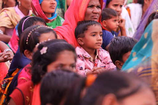 Woman in a headscarf and mask speaking to seated women in brightly colored traditional dresses during a session on personal hygiene.