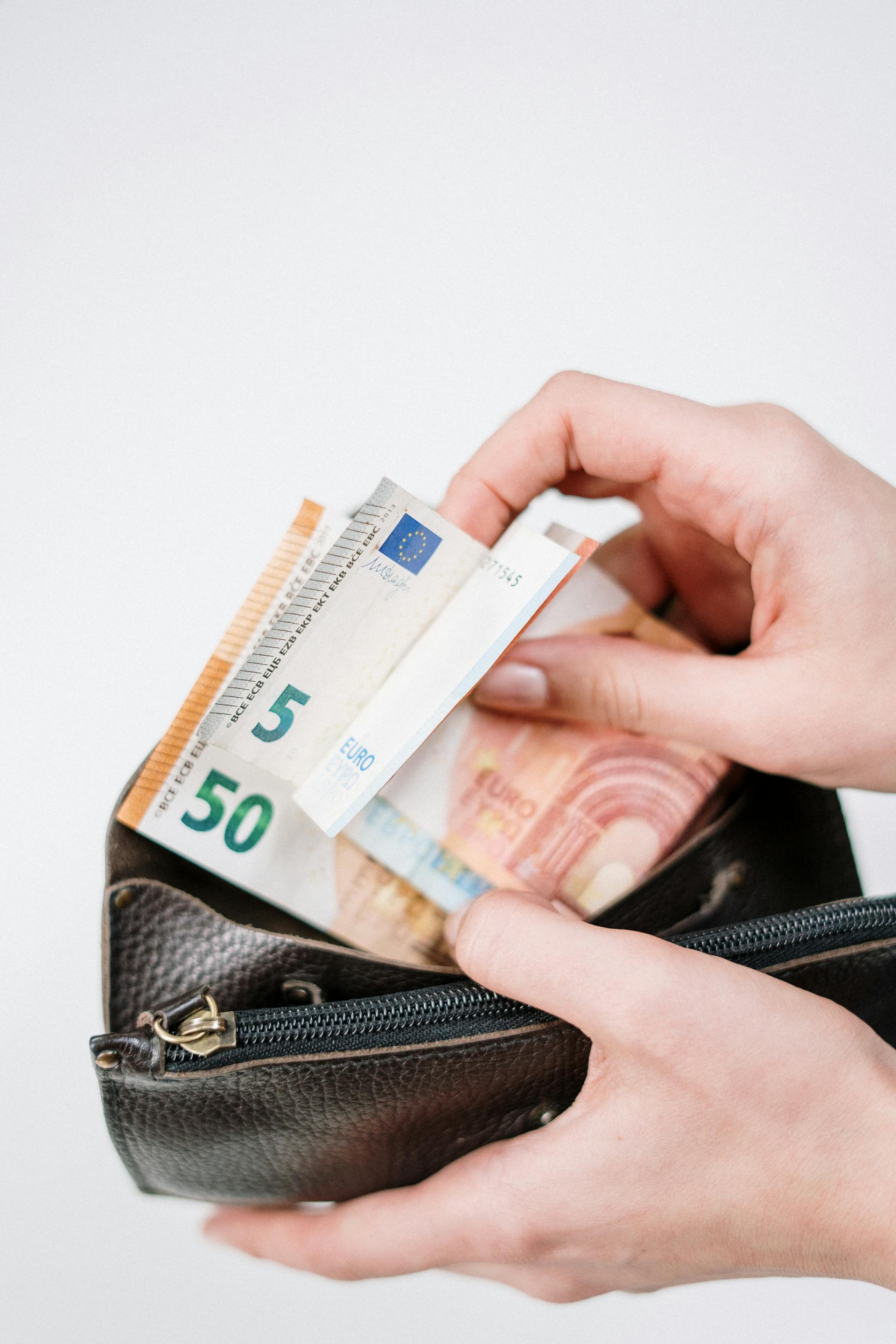 Hände halten eine schwarze Geldbörse mit Euro-Banknoten darin, darunter eine 50-Euro- und eine 5-Euro-Note.