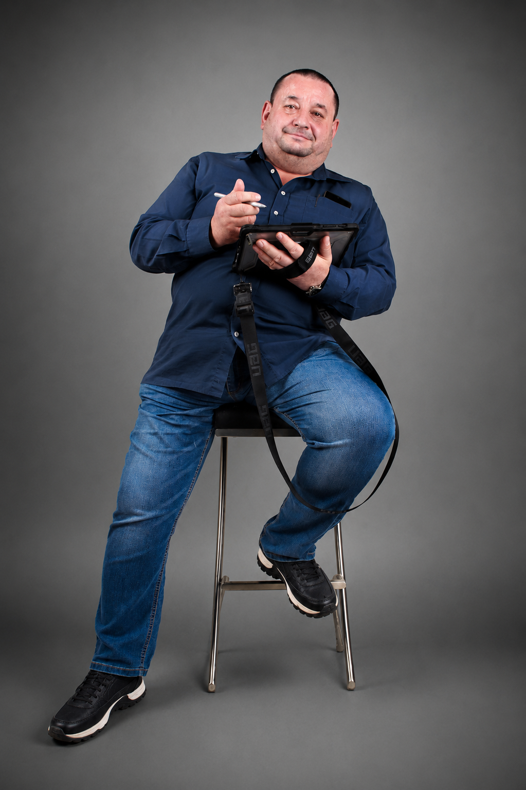 Mann mit blauem Hemd und Jeans sitzt auf Hocker und hält Tablet mit Stift.