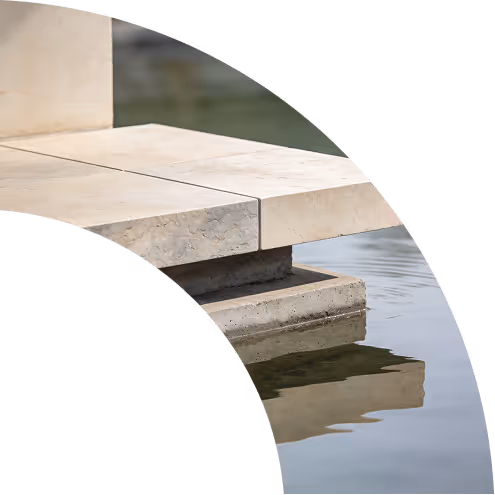 Close-up of a stone ledge with beige tiles extending over water reflecting its edge.