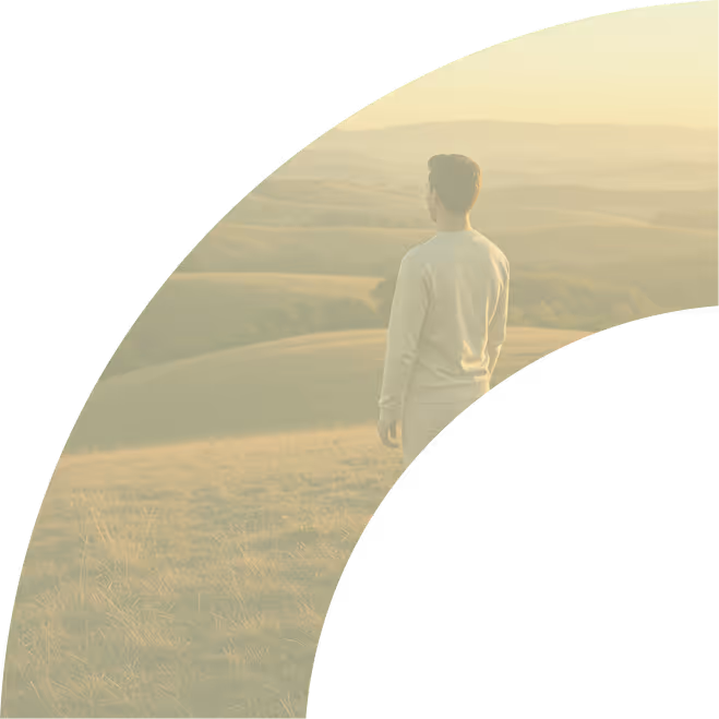 Man standing on a grassy hill looking at a vast landscape with rolling hills and distant mountains.