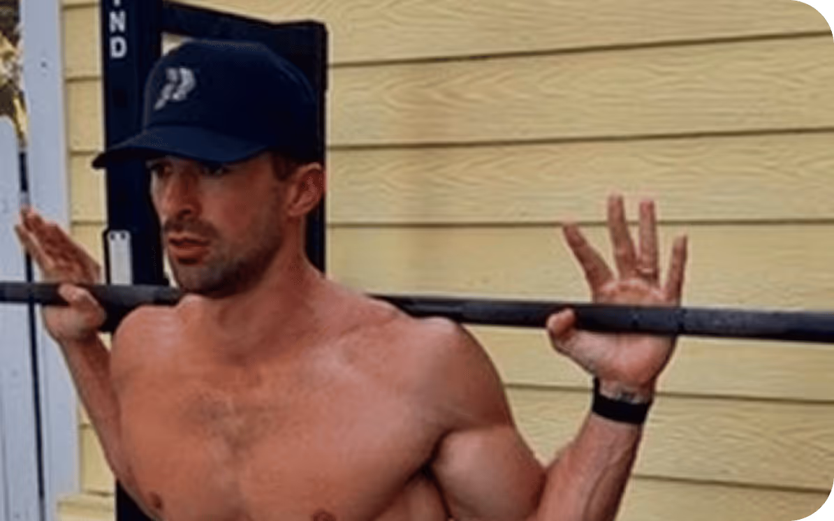 Dr. Moss wearing a black cap lifting a barbell against a yellow wall.