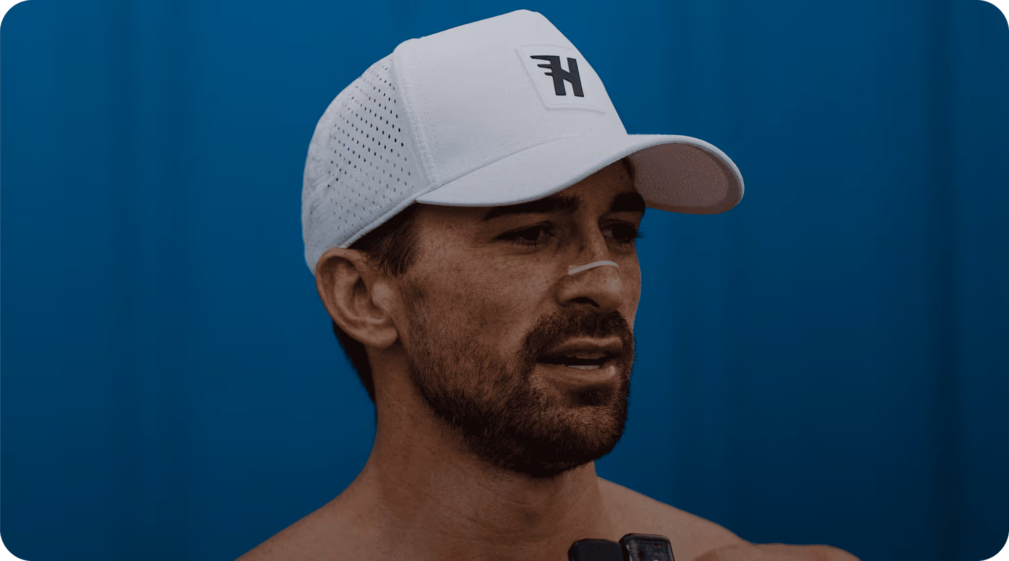 Dr. Clay Moss wearing a white cap with a black logo on a blue background.