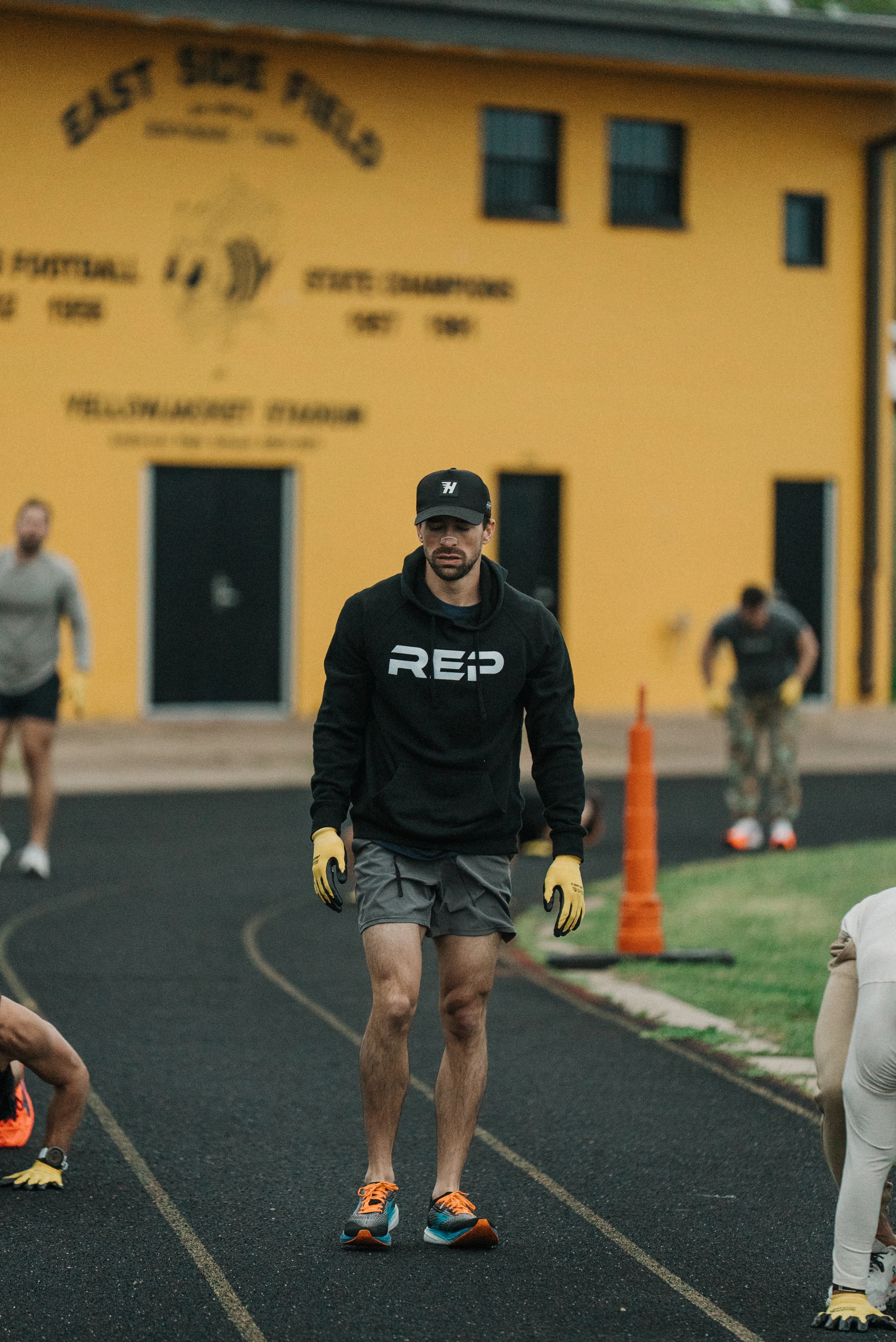 Dr. Moss in black hoodie and cap walking on a track field with other people exercising in the background.