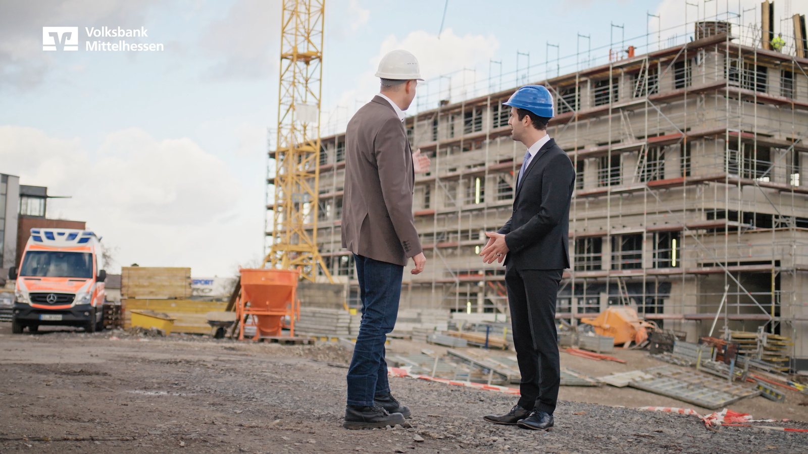 Zwei Personen mit Bauhelmen auf einer Baustelle vor der Kamera