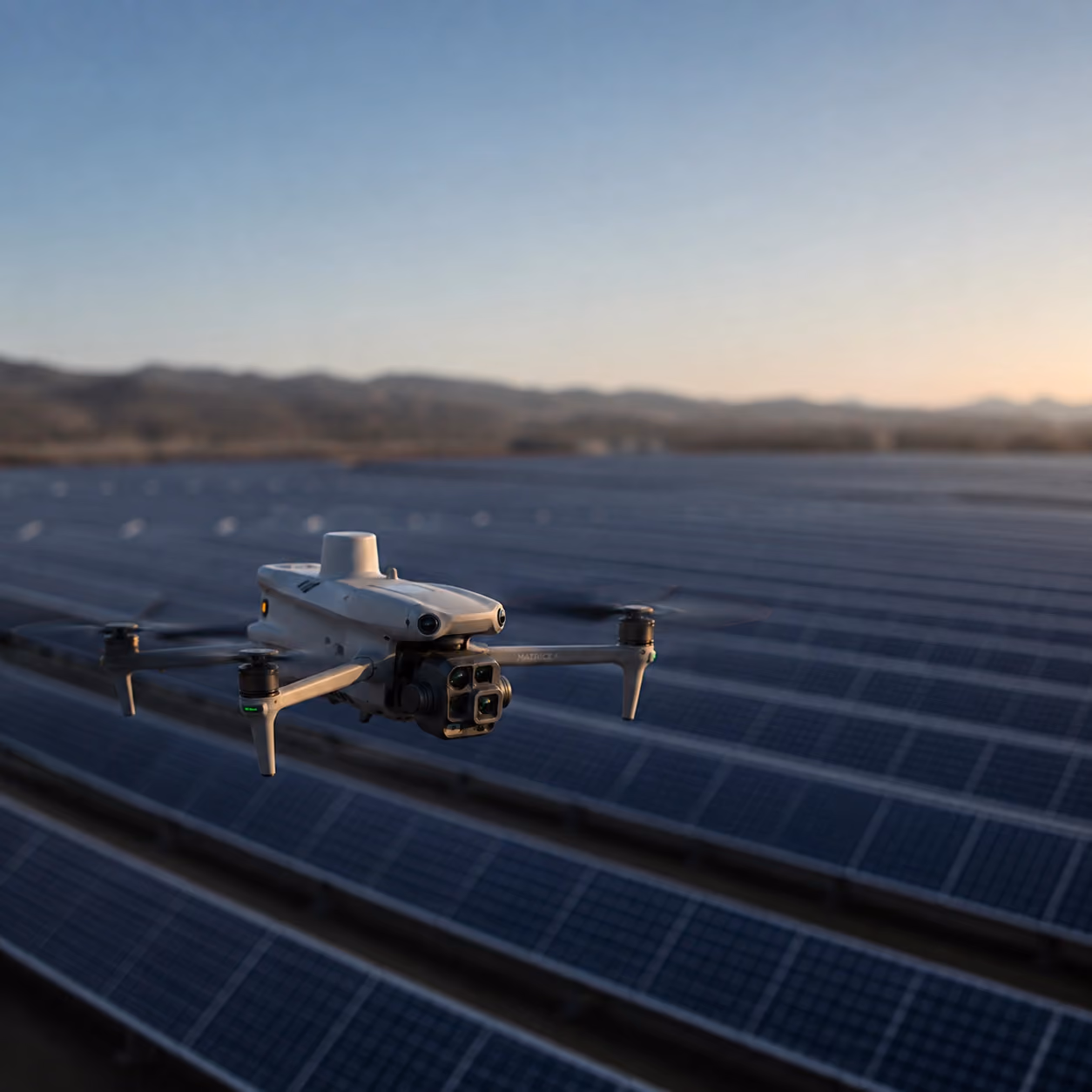 Drohne fliegt über ein großes Solarfeld bei Abendlicht mit Bergen im Hintergrund.