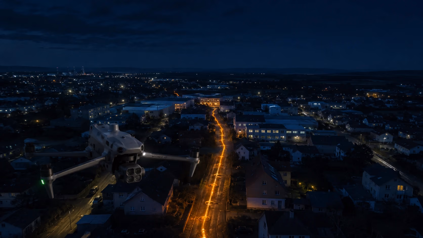 Drohne fliegt nachts über eine Stadtstraße mit hellen orangen Lichtern in der Mitte.