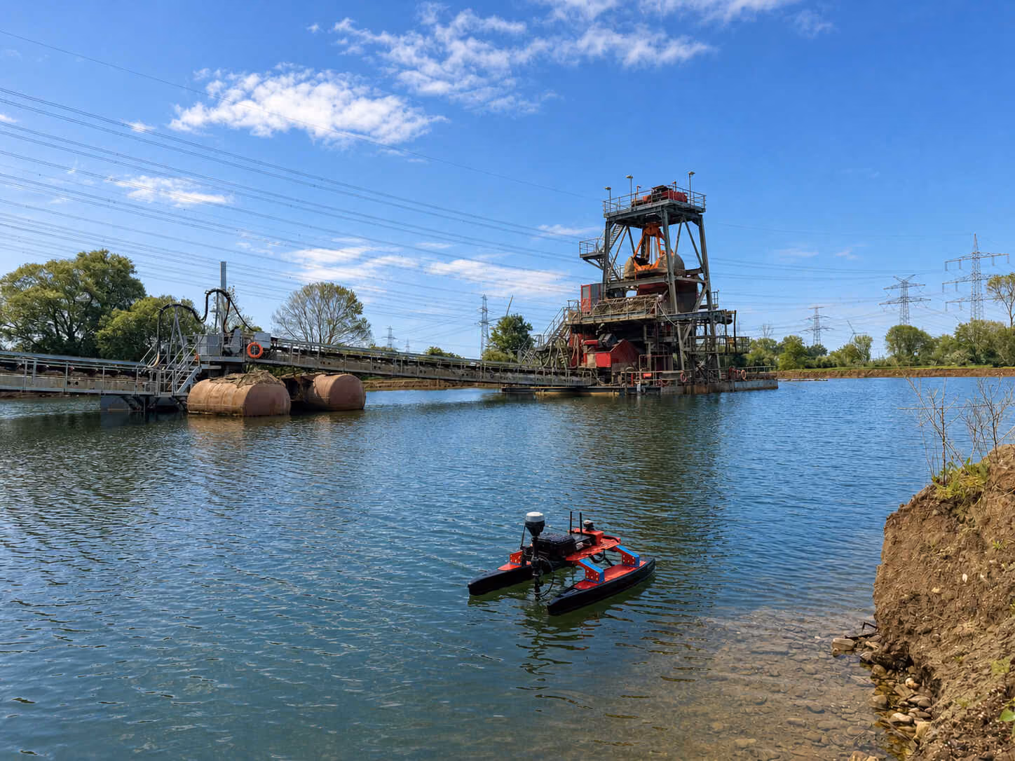 Rotes Echolotboot bei der Gewässervermessung auf einem Baggersee vor einer Kieswerksanlage.