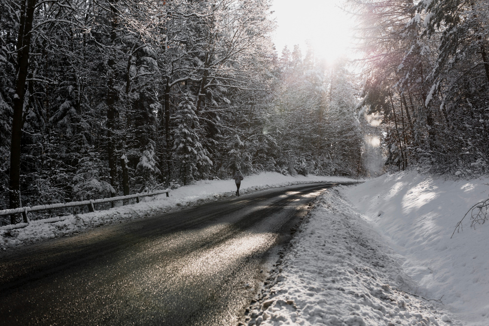 Verschneite Waldstraße im Winter mit Sonnenlicht zwischen den Bäumen